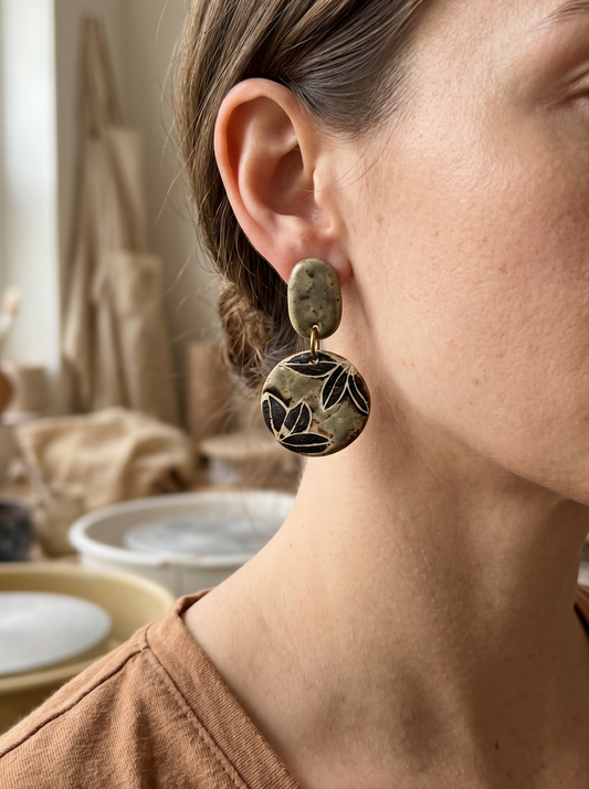 Side profile of a model wearing HECROWN chunky sage green ceramic earrings with dark engraved botanical patterns. A unique piece of wearable art and a sincere handcrafted gift.