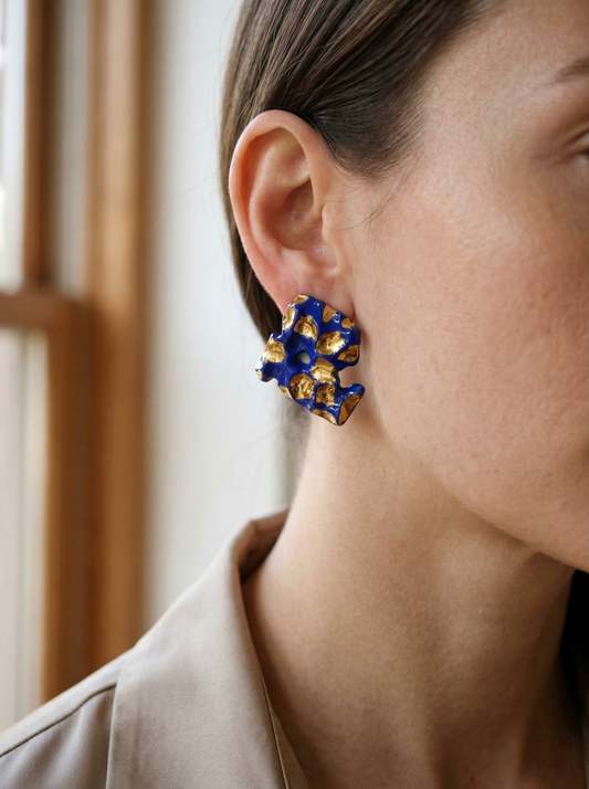Side profile of a model wearing HECROWN 004 organic-shaped ceramic stud earrings with deep cobalt blue and liquid gold glaze. Captured in soft natural window light to highlight the sculptural texture and handcrafted detail of Jingdezhen artisan jewelry