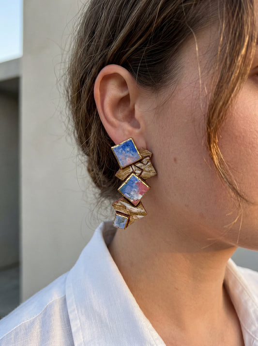 Side view of a model wearing HECROWN 003 geometric ceramic earrings with layered blue and pink abstract squares. Styled with a crisp white linen shirt in natural daylight to showcase the sculptural elegance and wearable art aesthetic from Jingdezhen