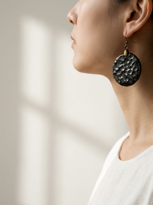 Side profile of a model wearing HECROWN chunky black hammered ceramic earrings. A bold, wabi-sabi statement piece perfect for a unique anniversary gift.