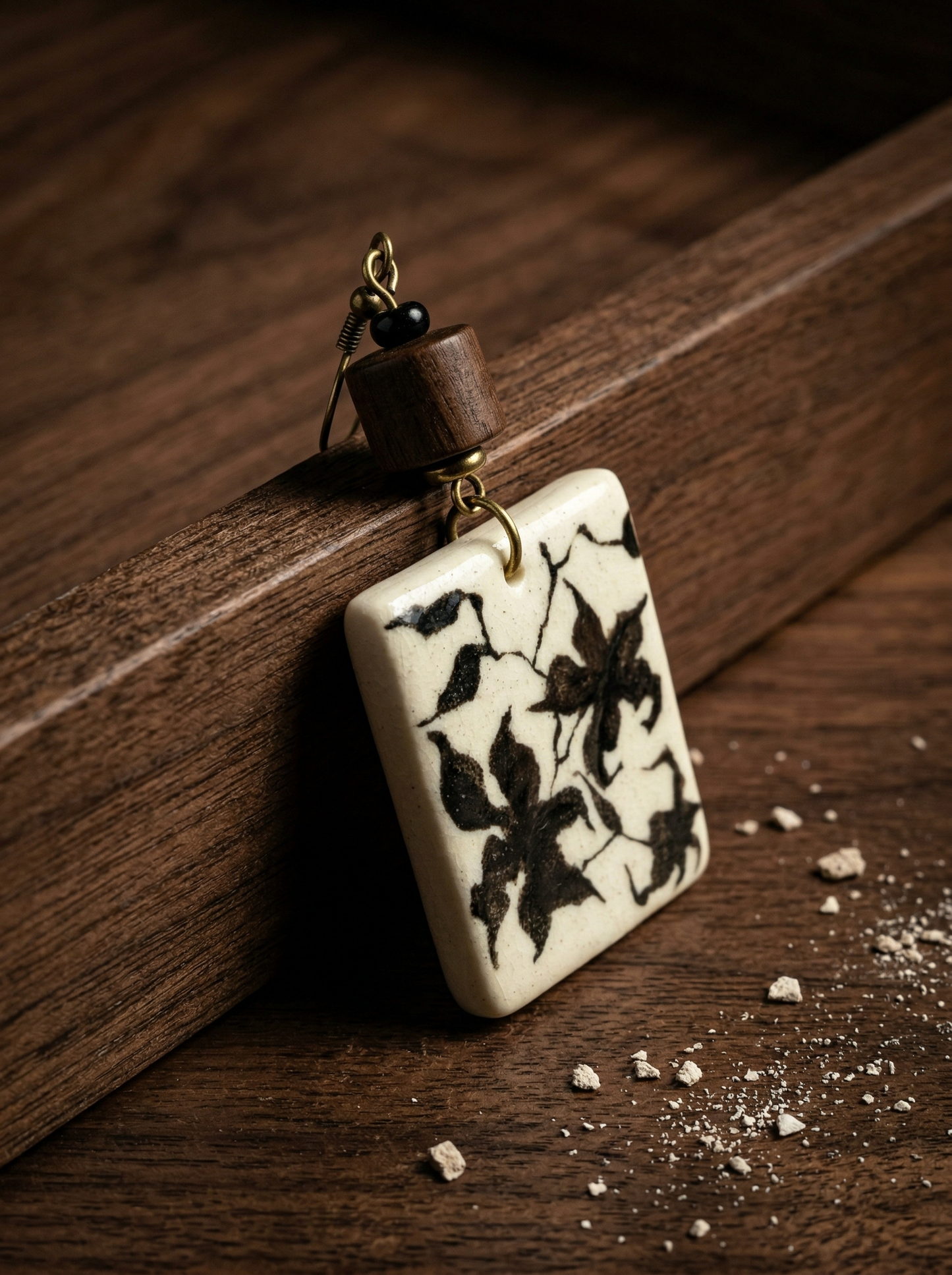 Close-up of a HECROWN painted porcelain earring resting on wood with scattered ceramic dust. A raw and sincere display of Jingdezhen handmade jewelry, perfect for a unique anniversary gift.