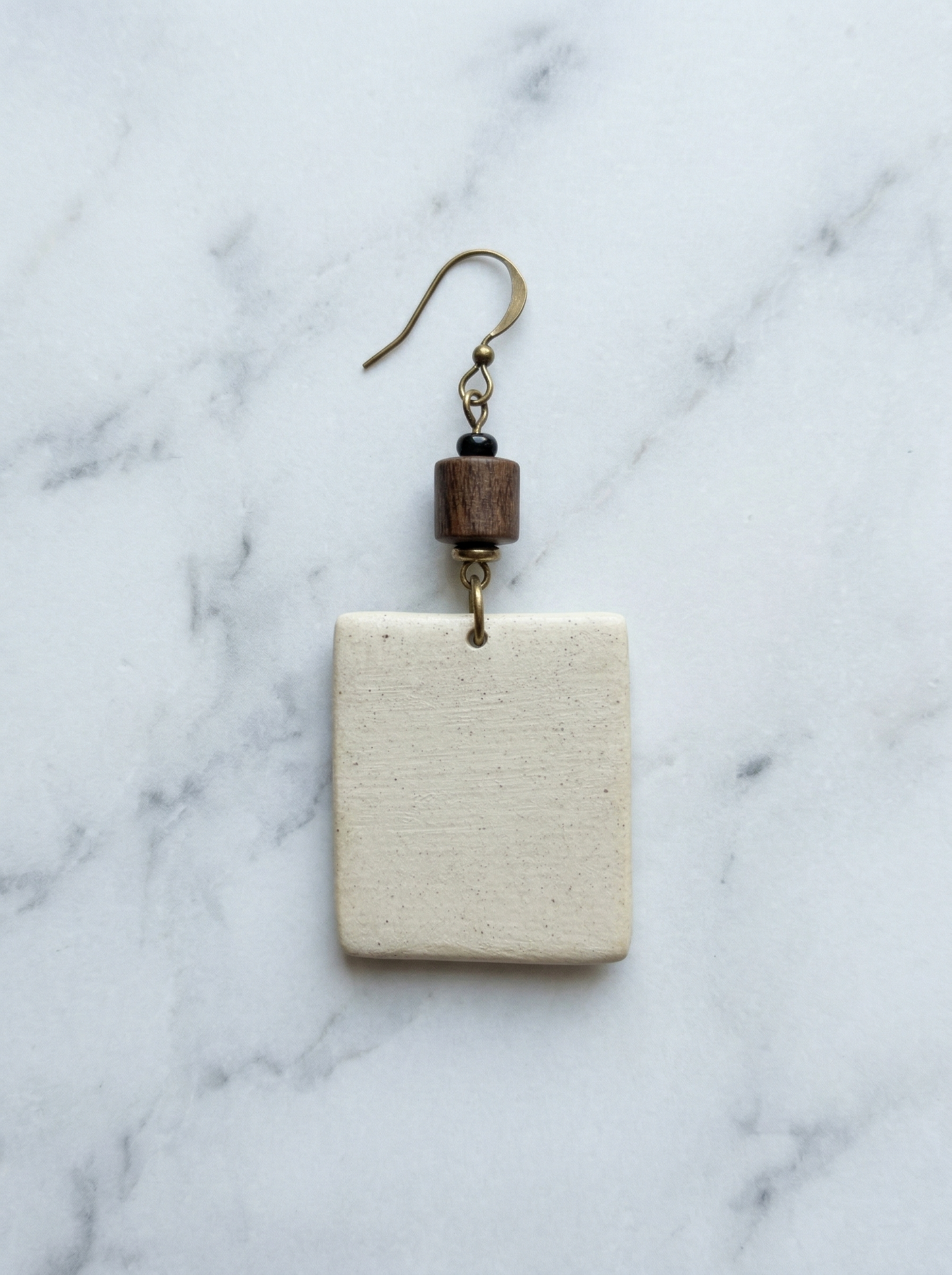 Reverse side of a HECROWN ceramic earring on white marble, showing the raw, unglazed porcelain texture. Transparent physical details verifying the sincere Jingdezhen handcrafted jewelry process.