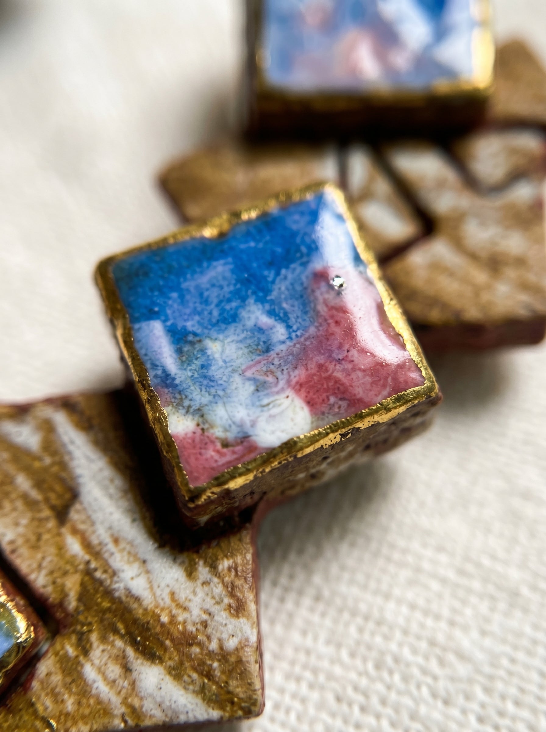 Extreme macro shot of the 003 geometric ceramic earring, revealing the intricate flow of blue and pink glazes and gold-rimmed edges. Every physical detail captures the concentration and sincere craftsmanship of the Jingdezhen artisan, emphasizing the unique, non-replicable nature of 1-of-1 wearable art.