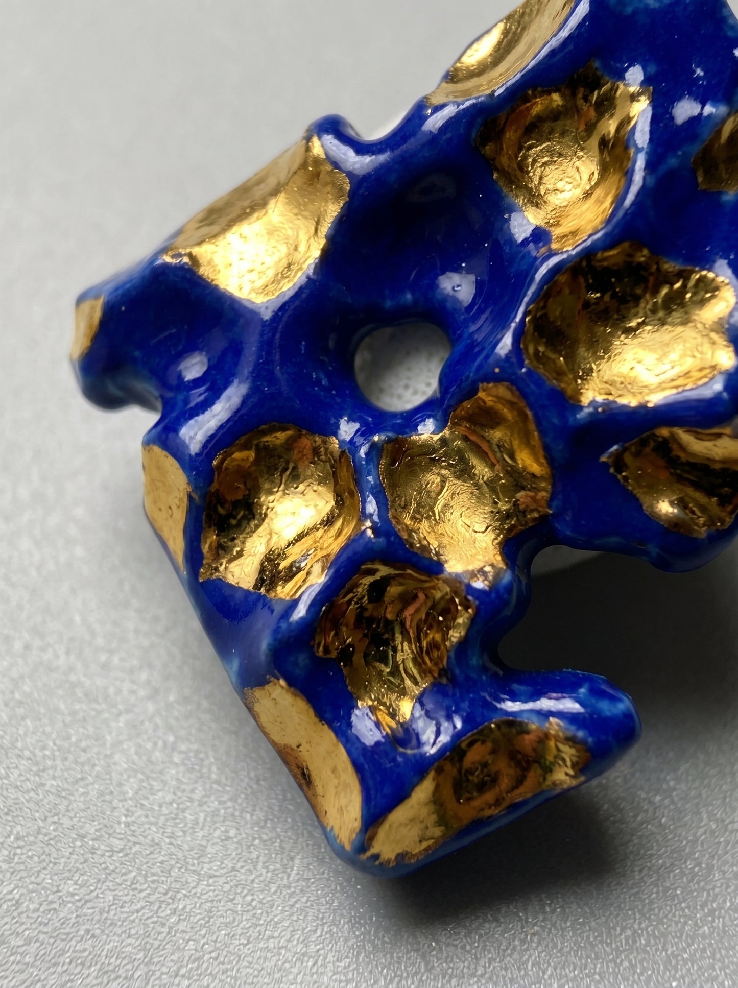 Extreme macro close-up of a HECROWN organic ceramic earring, showcasing the vibrant cobalt blue glaze and liquid gold accents within hand-sculpted hollows. Every physical detail reflects the concentration and sincere craftsmanship from the Jingdezhen studio.