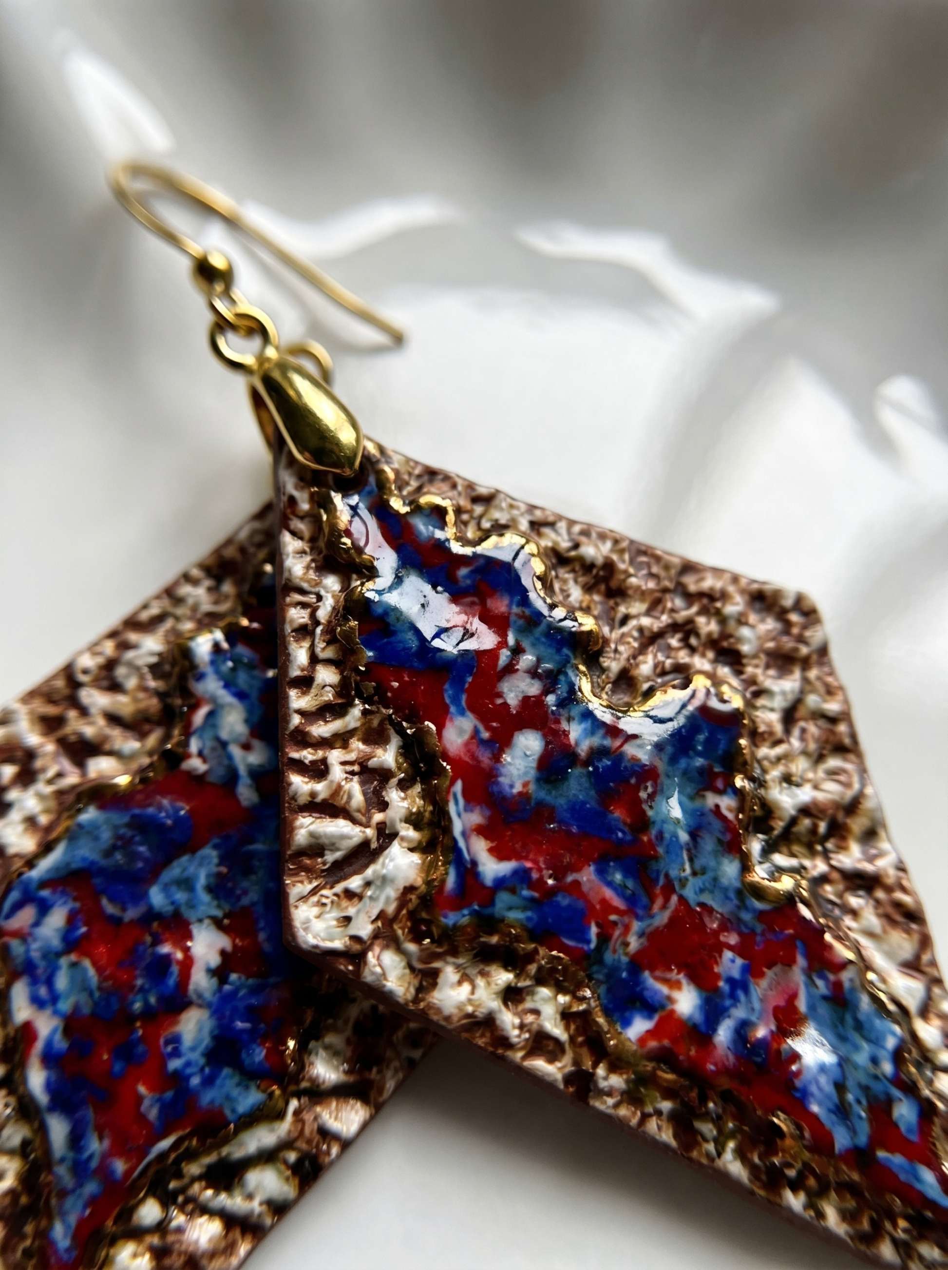 Extreme macro shot of HECROWN 005 rhombus ceramic earring, showing the intricate bronze-like textured surface and the vibrant flowing blue and red glazes. The focused physical details highlight the sincere handcrafted quality and concentration of the Jingdezhen artisan.