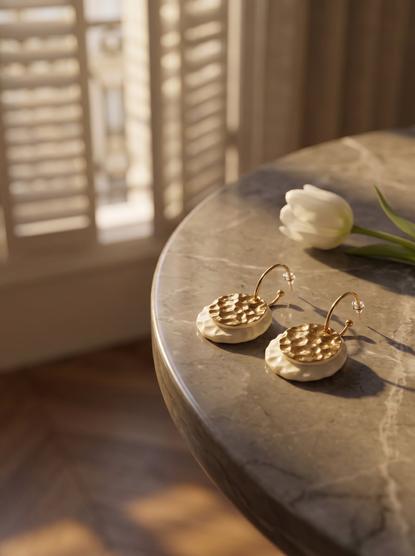 HECROWN 006 earrings on a marble table with a white tulip, captured in warm morning sunlight to highlight the realistic physical details and handmade warmth.