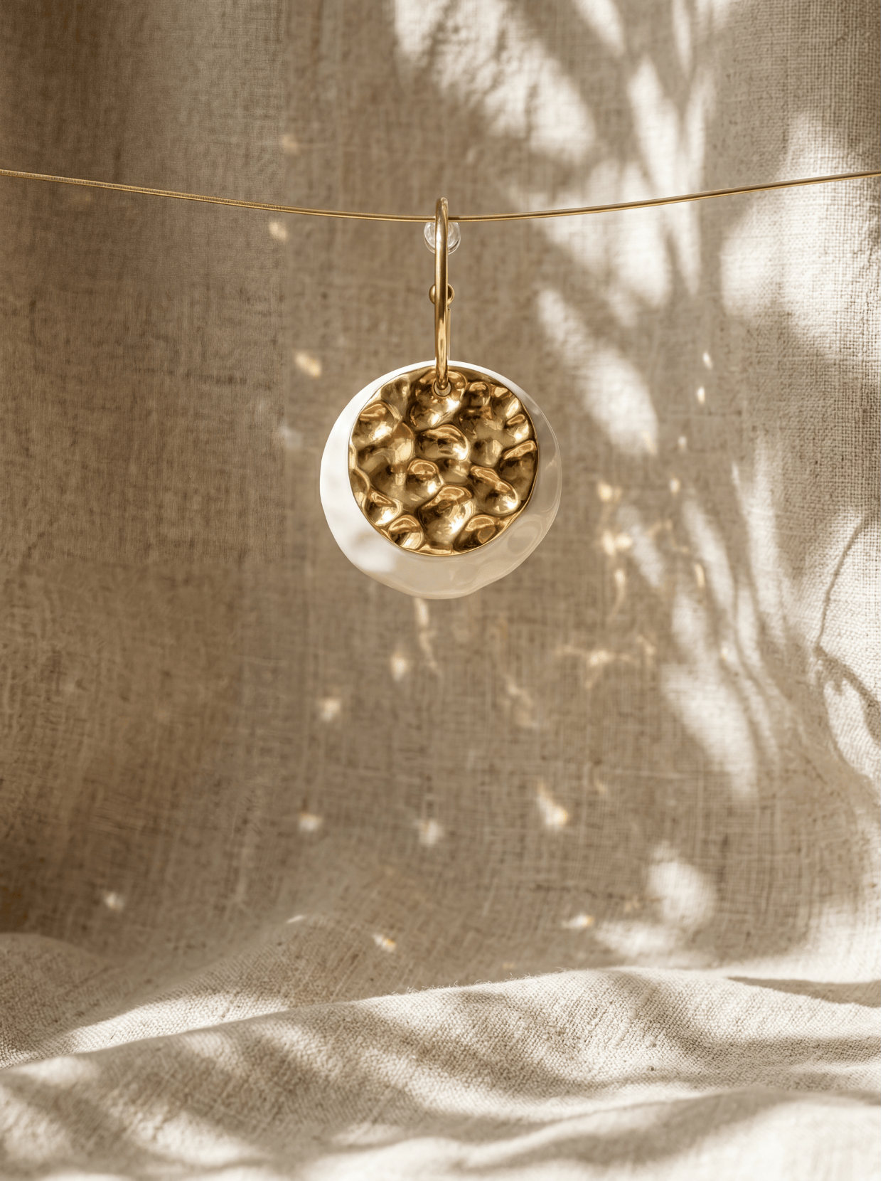 A single HECROWN 006 ceramic earring suspended against a linen backdrop with botanical shadows, showcasing a blend of modern design and oriental Zen aesthetic.