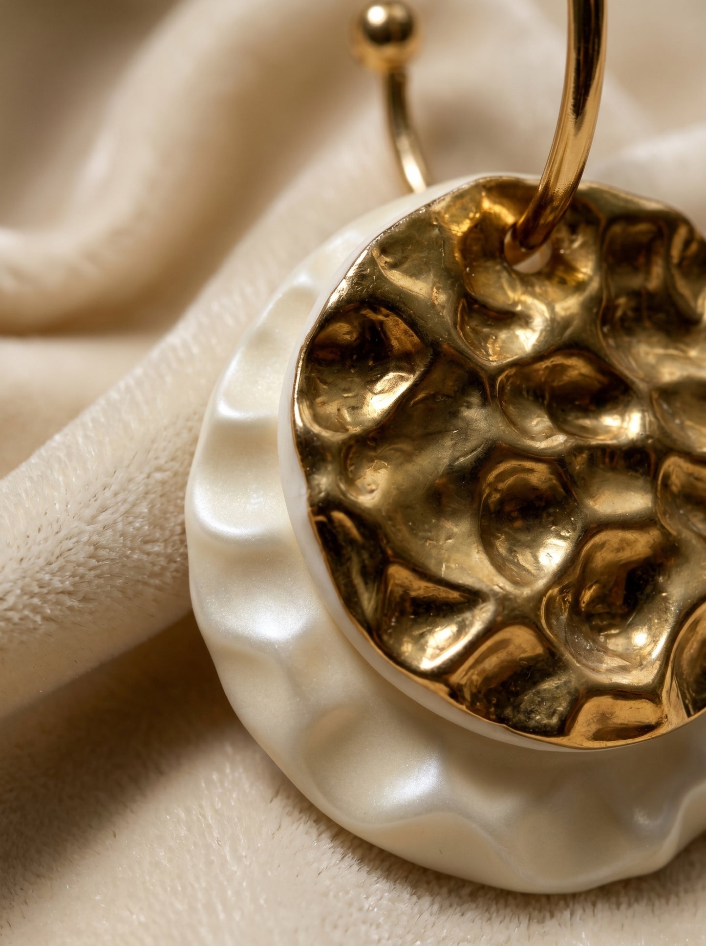 An extreme macro close-up of the HECROWN 006 ceramic earring, focusing on the golden hammered texture and wavy white porcelain edge against a soft cream velvet background. Highlighting the realistic physical details and handcrafted sincerity from the Jingdezhen studio.