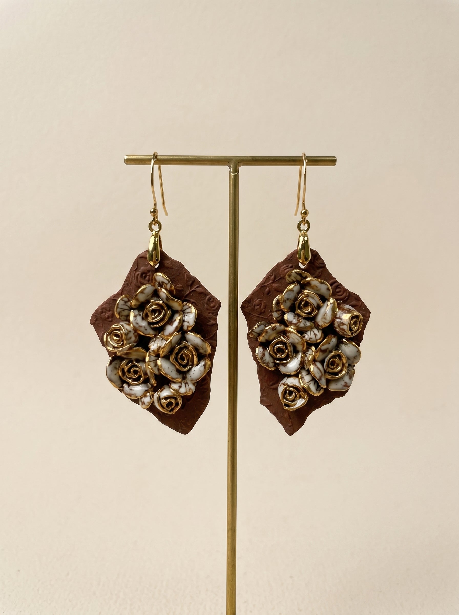 HECROWN 007 Ruined Rose ceramic earrings displayed on a minimalist gold stand. Highlighting the sculptural quality and the sincere handmade spirit of Jingdezhen.