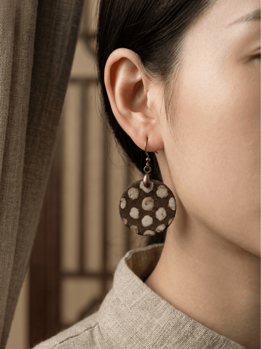 Side profile of a model wearing HECROWN round brown crackle polka dot ceramic earrings. A unique piece of everyday wearable artisan jewelry from Jingdezhen.