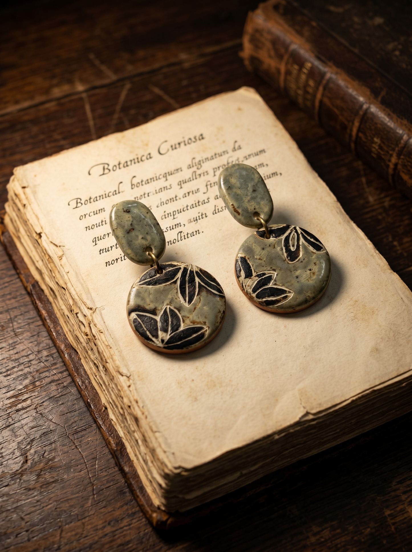 HECROWN carved botanical ceramic earrings resting on an antique Botanica Curiosa book. Perfect for lovers of dark academia and sincere Jingdezhen ceramic art.