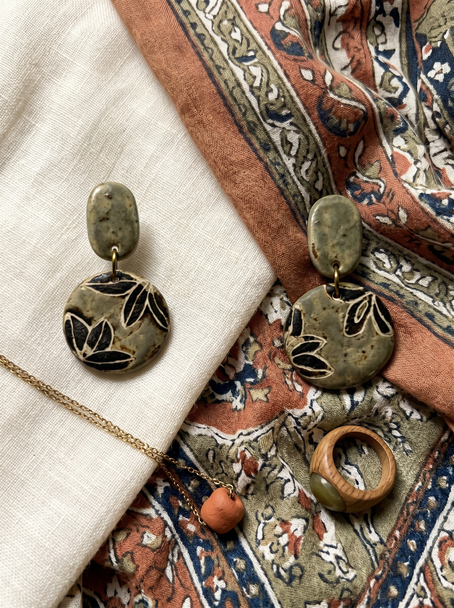 HECROWN celadon green ceramic botanical drop earrings displayed on patterned fabric with a matching ring and pendant. Authentic Jingdezhen handmade jewelry set.
