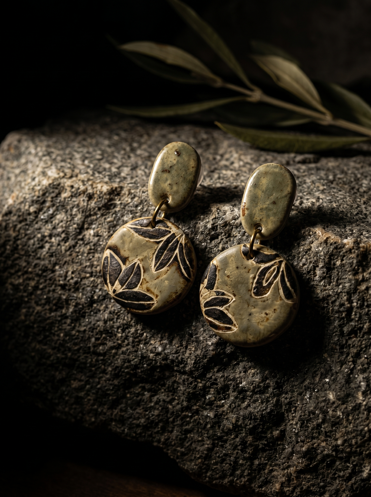 A pair of HECROWN celadon green ceramic drop earrings with carved botanical leaf motifs resting on a dark stone. Authentic Jingdezhen handmade jewelry with a vintage aesthetic.