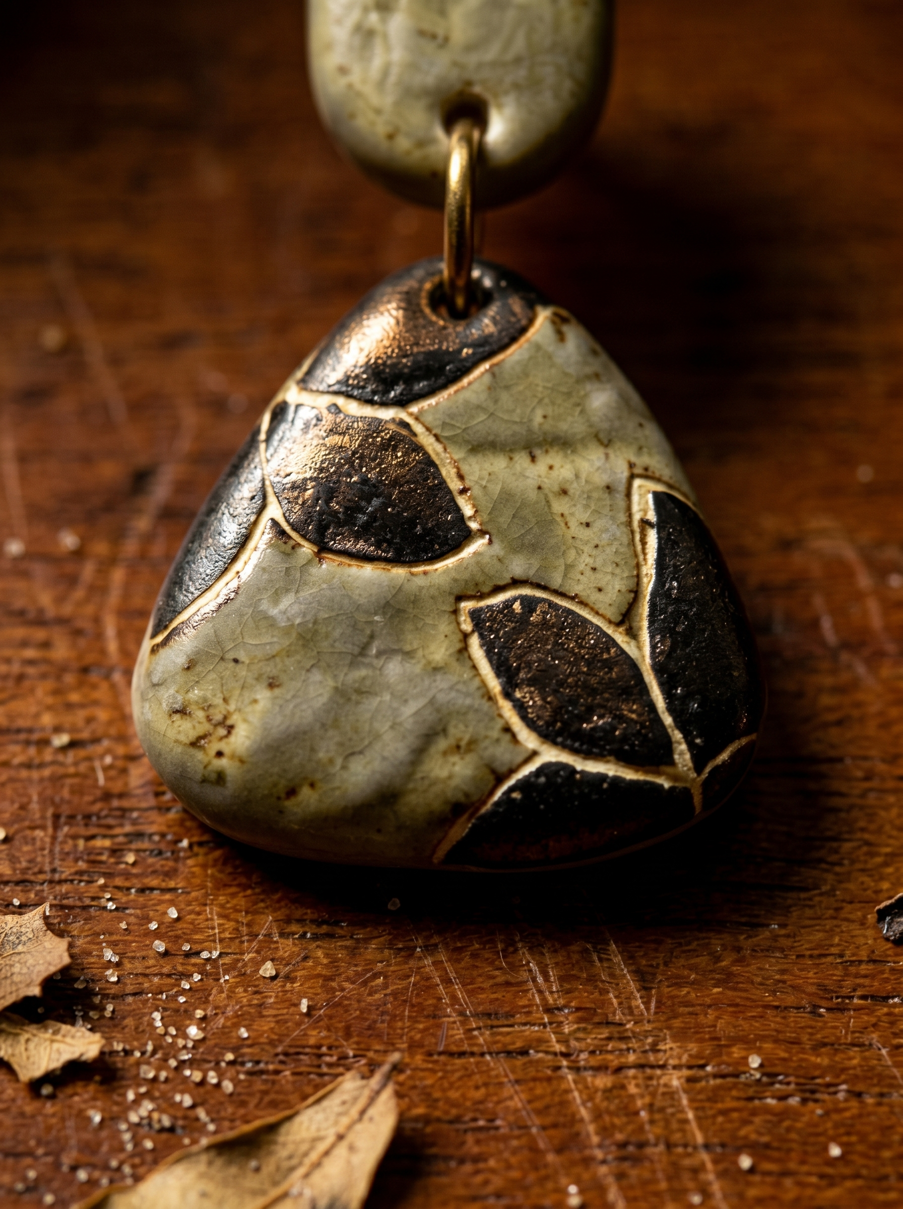 Extreme macro close-up of a HECROWN celadon ceramic earring on dark wood, highlighting the dark inlaid botanical carving and authentic Jingdezhen craftsmanship.