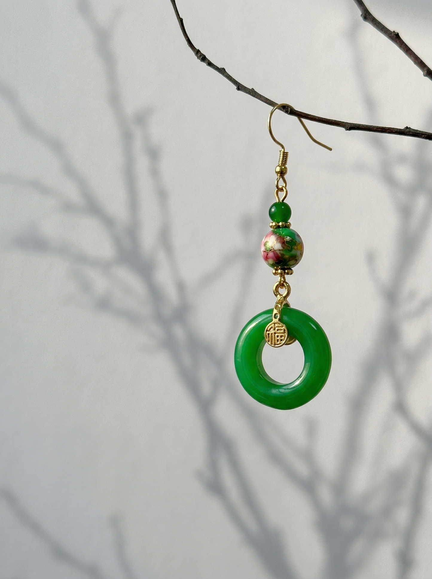 A single HECROWN green ceramic earring hanging from a tree branch with soft shadows. Nature-inspired handmade ceramic gift and a unique anniversary gift.