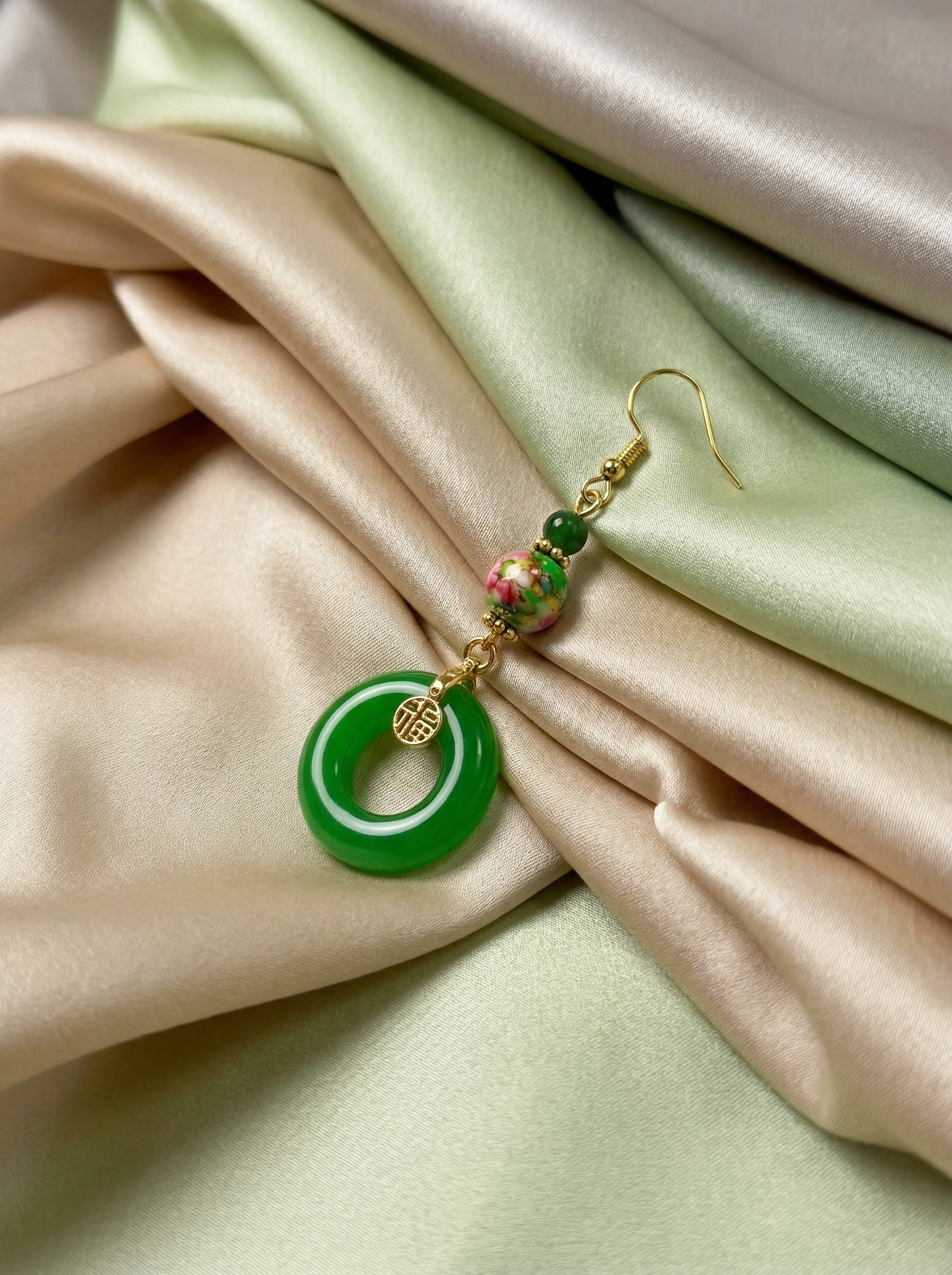 HECROWN green ceramic earring resting on flowing silk fabric. A luxurious lifestyle shot perfect for a unique Valentine's Day gift for her.