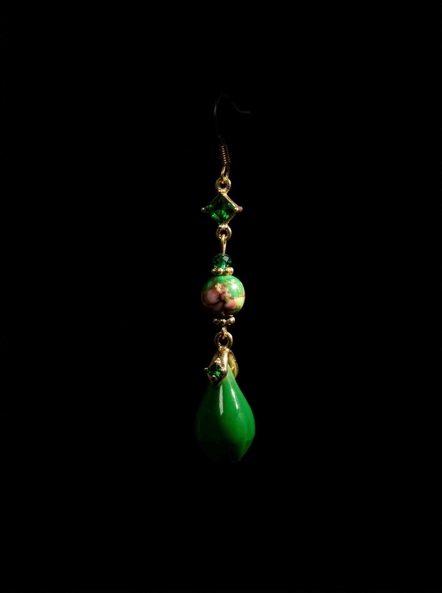 A single HECROWN emerald green ceramic teardrop earring suspended against a dark background. Emphasizing the vibrant glaze of handcrafted porcelain jewelry.
