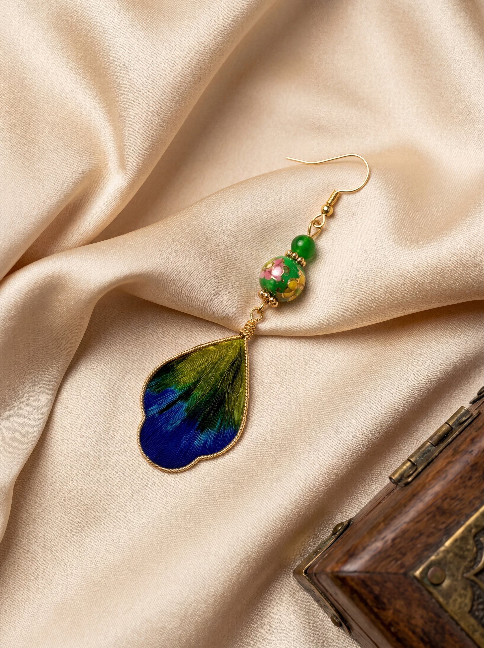 HECROWN silk wing earring resting on linen next to a vintage wooden box. A perfect Valentine's Day gift featuring authentic artisan craftsmanship.