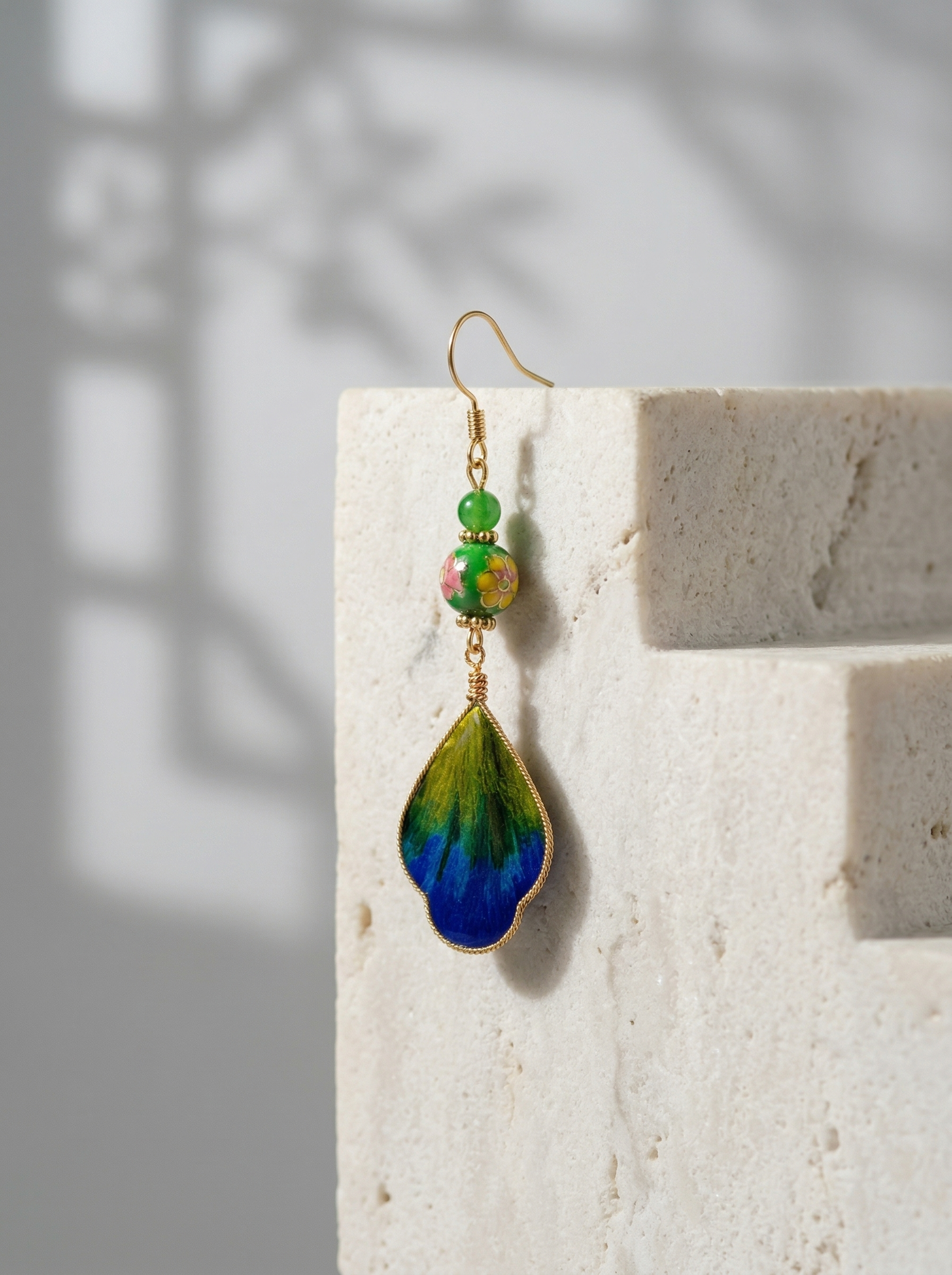 HECROWN handcrafted silk and porcelain feather earring on a white architectural pedestal. Elegant Jingdezhen ceramic jewelry for modern lifestyle.