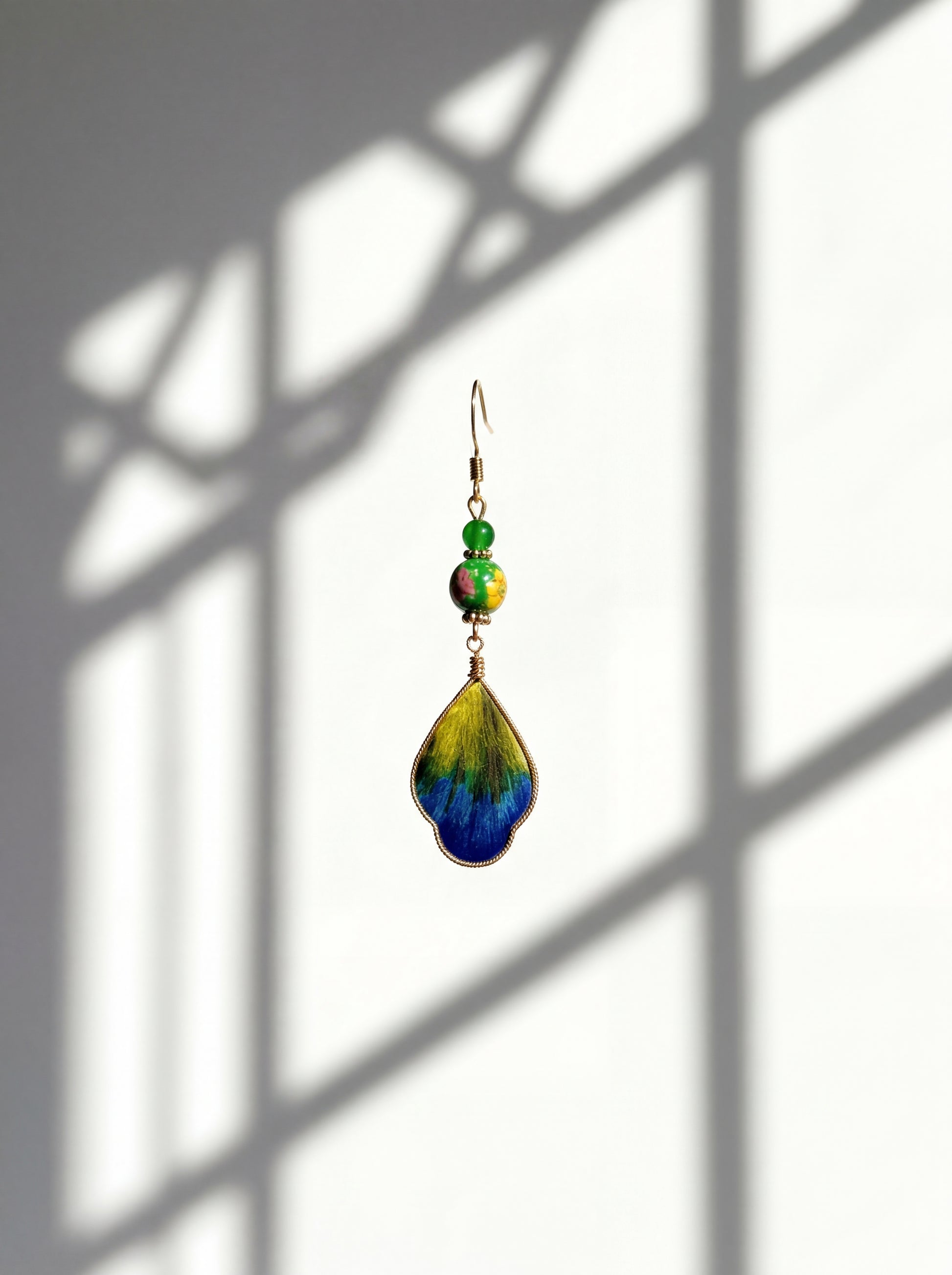 HECROWN handcrafted silk wing earring against a white wall with traditional window shadows. A soulful piece of Jingdezhen porcelain art.