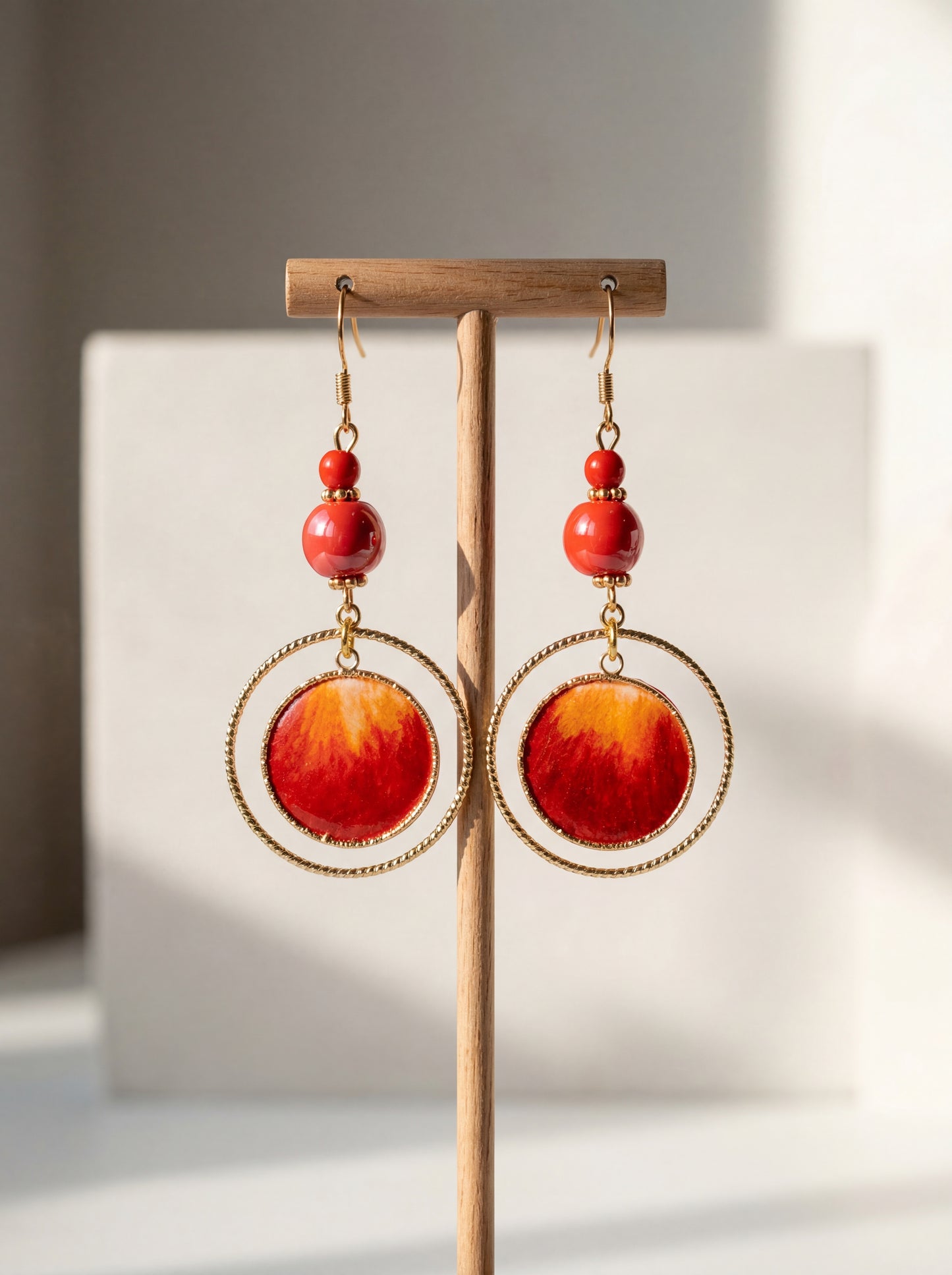 A pair of HECROWN 020 fiery red sun earrings made of ceramic and silk, displayed on a wooden stand. Sincere Jingdezhen handmade jewelry.