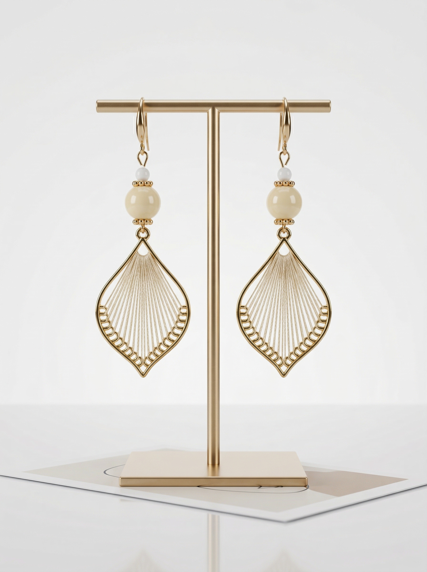 A pair of HECROWN 021 cream ceramic and silk weaving earrings on a gold T-stand. Minimalist Jingdezhen handmade jewelry.