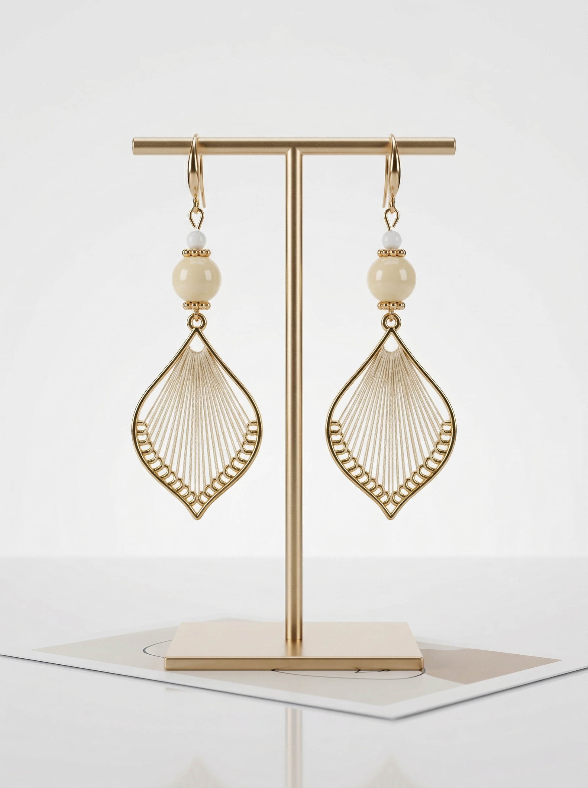 A pair of HECROWN 021 cream ceramic and silk weaving earrings on a gold T-stand. Minimalist Jingdezhen handmade jewelry.