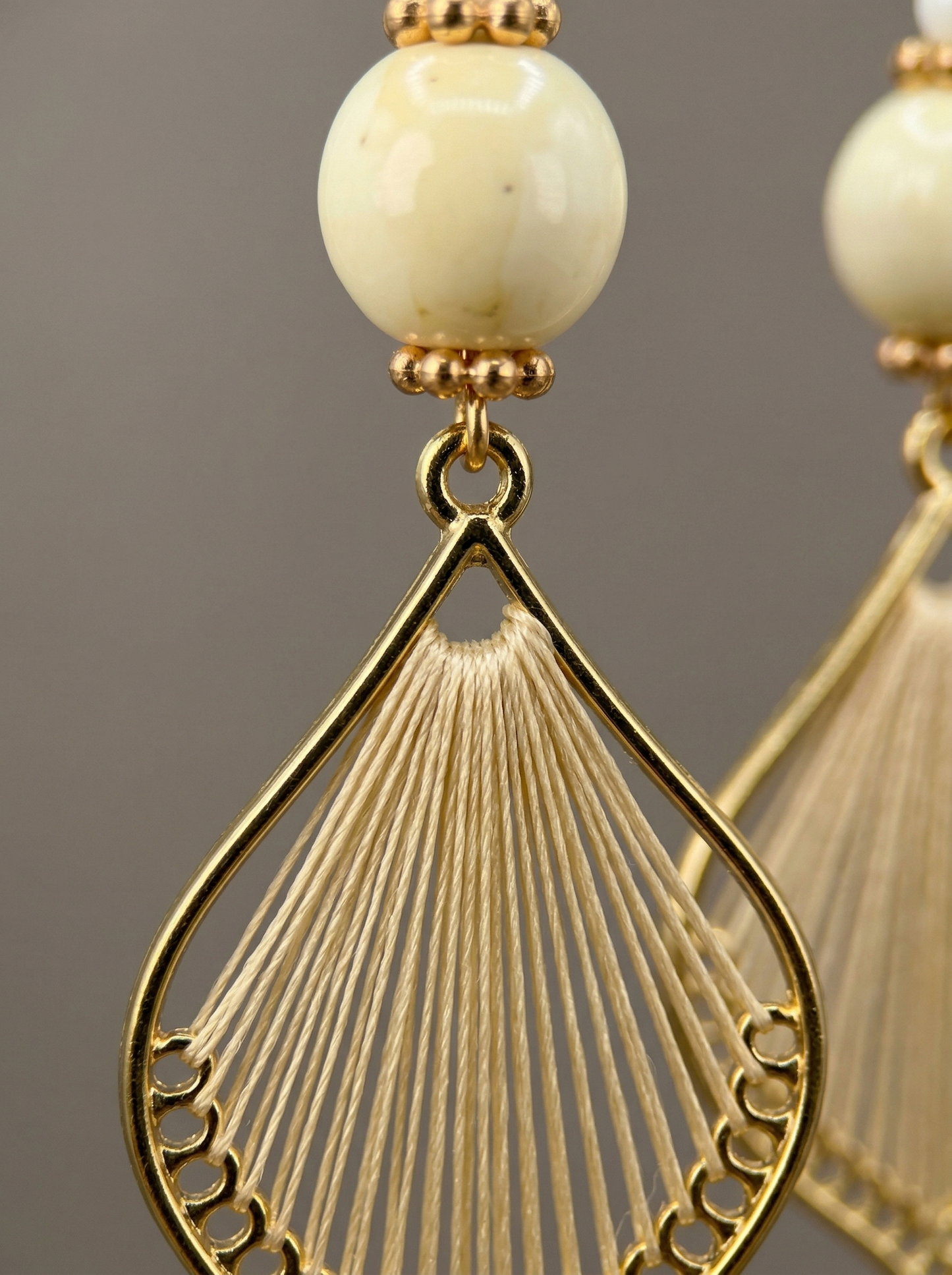 Extreme macro shot of HECROWN earring, focusing on the fine silk threads and the smooth cream ceramic bead. Authentic artisan craftsmanship.