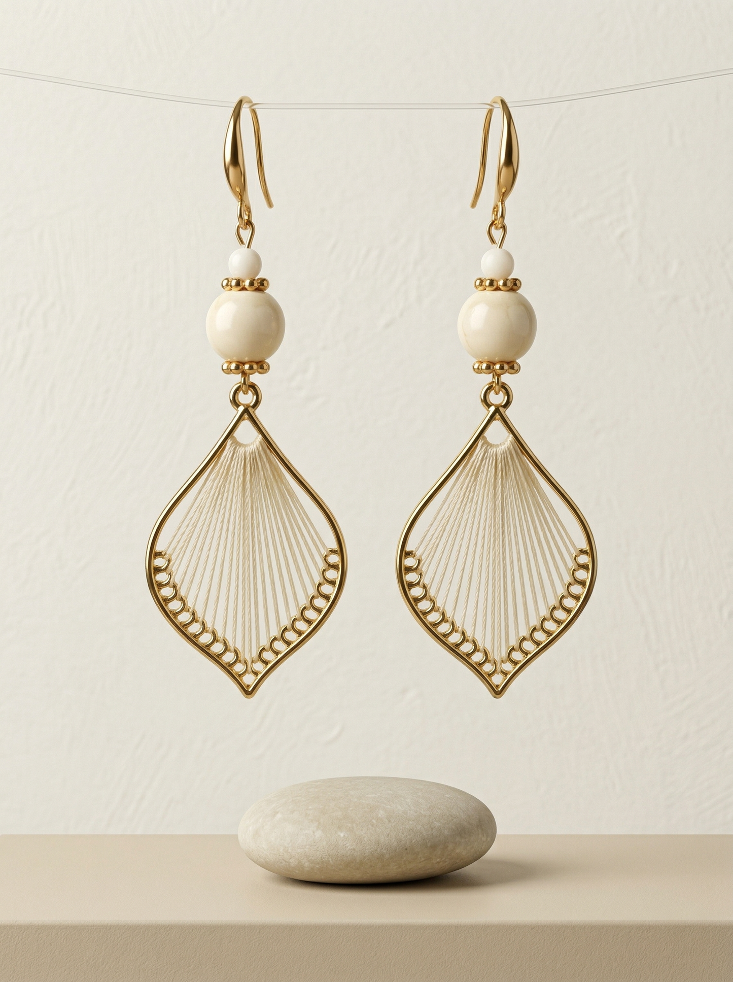 HECROWN cream silk and porcelain earrings hanging over a small stone. Showcasing the pure and sincere handcrafted gift aesthetic.