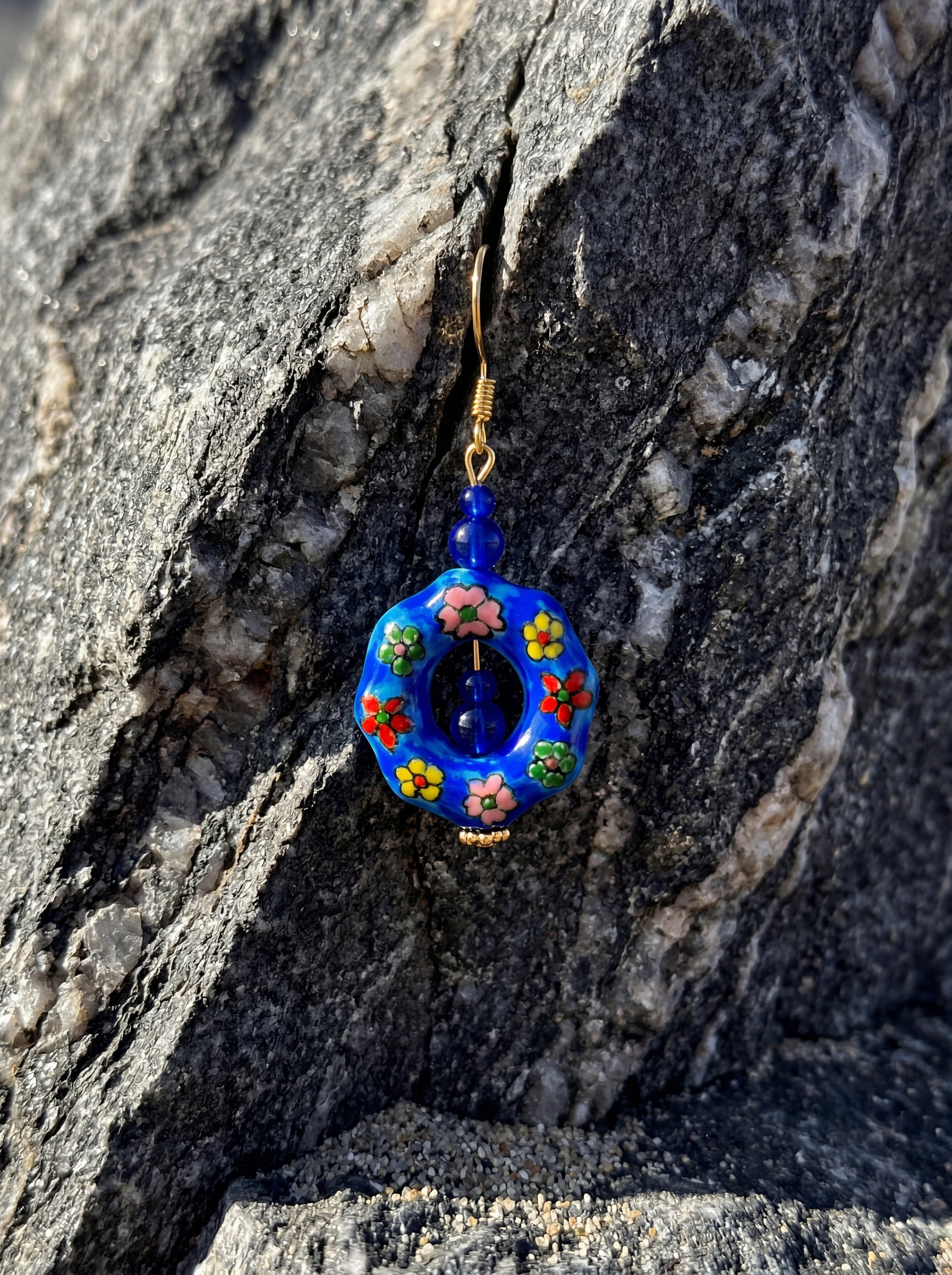 HECROWN blue ceramic earring resting on a dark volcanic rock with moss. Showcasing the sincere wabi-sabi handmade jewelry aesthetic.