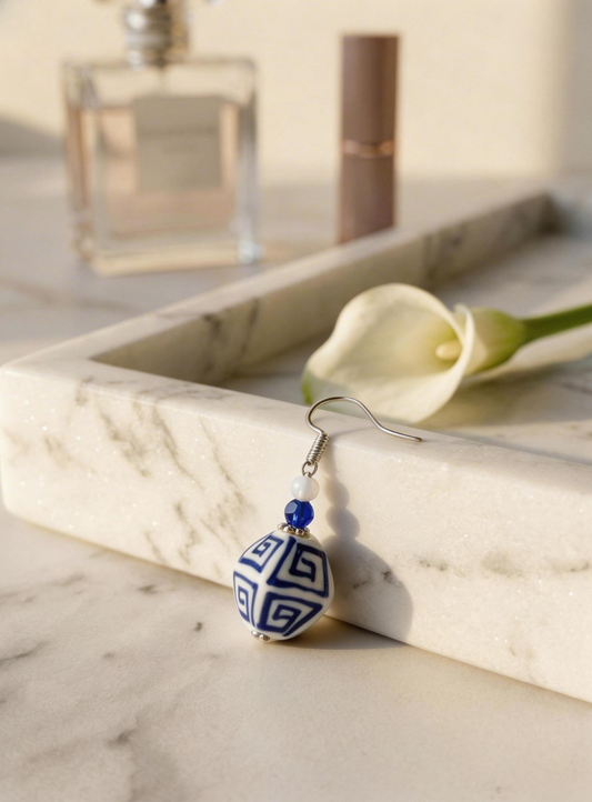 A single HECROWN cobalt blue ceramic hoop earring with hand-painted mini flowers hanging from a branch. Unique Jingdezhen handmade jewelry.