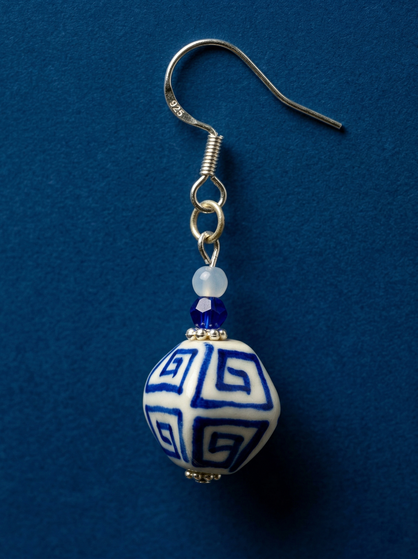 HECROWN hand-painted blue ceramic earrings on an open book next to a coffee cup. A warm lifestyle shot of Jingdezhen handmade jewelry.
