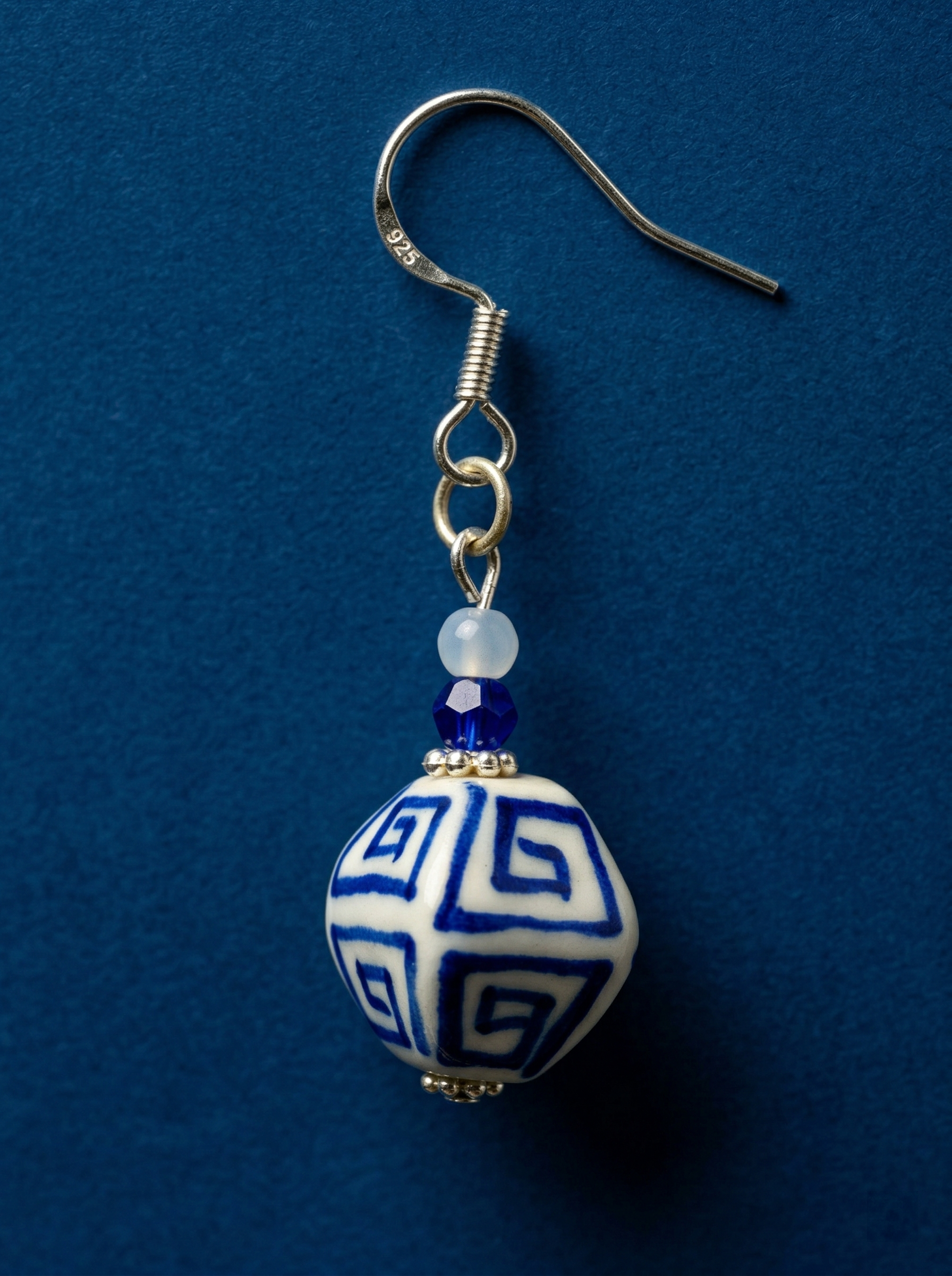 HECROWN hand-painted blue ceramic earrings on an open book next to a coffee cup. A warm lifestyle shot of Jingdezhen handmade jewelry.