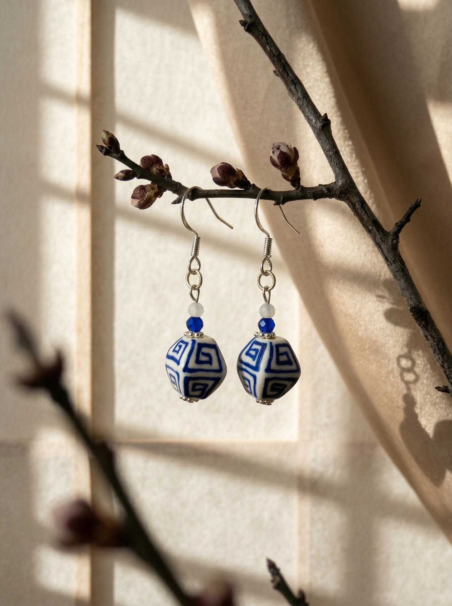 HECROWN hand-painted blue ceramic earring on a gold T-stand against a clean background. Authentic handcrafted porcelain jewelry.