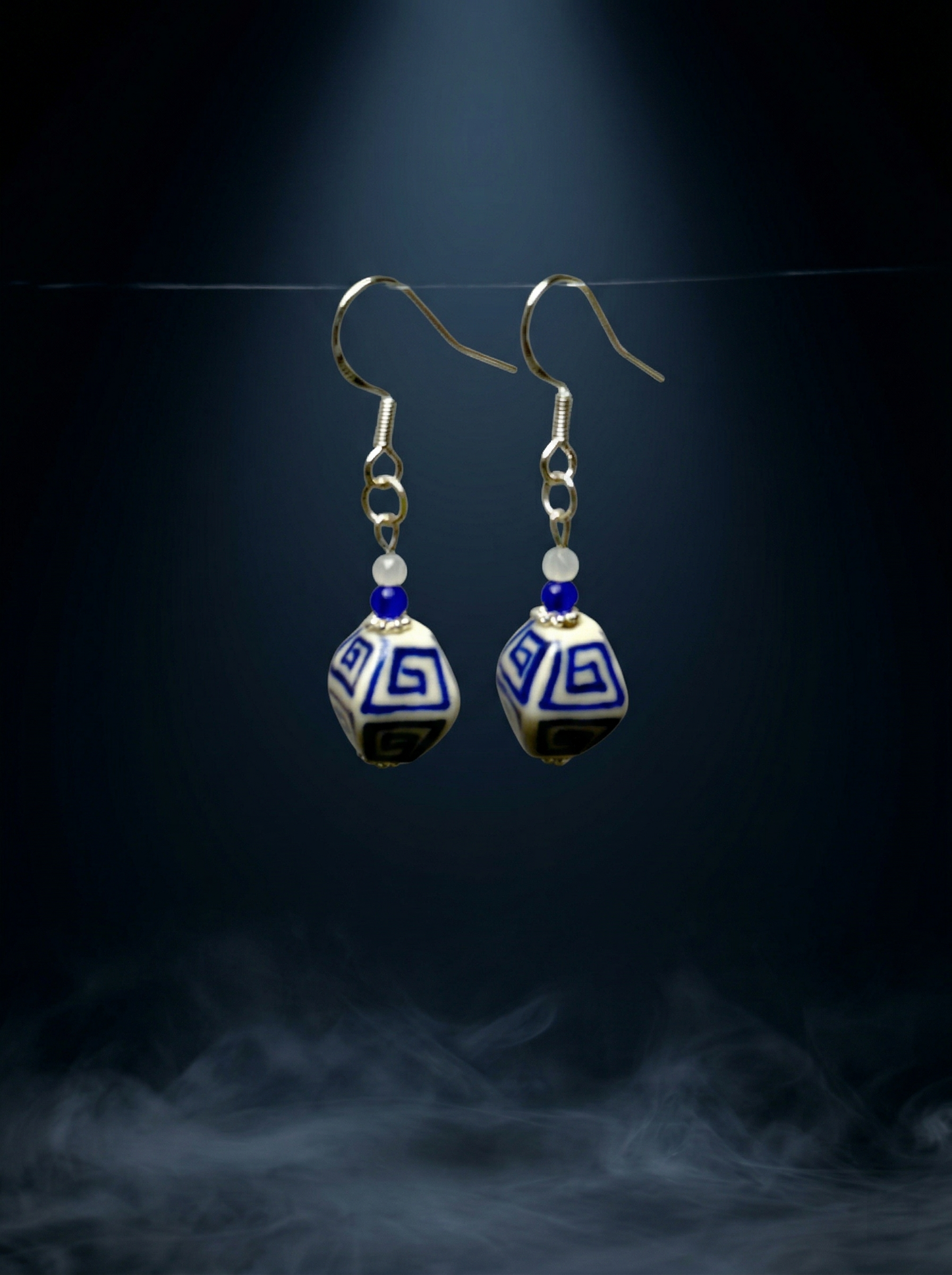 HECROWN blue floral ceramic earring resting on a dark volcanic rock with moss. Showcasing the sincere wabi-sabi handmade jewelry style.