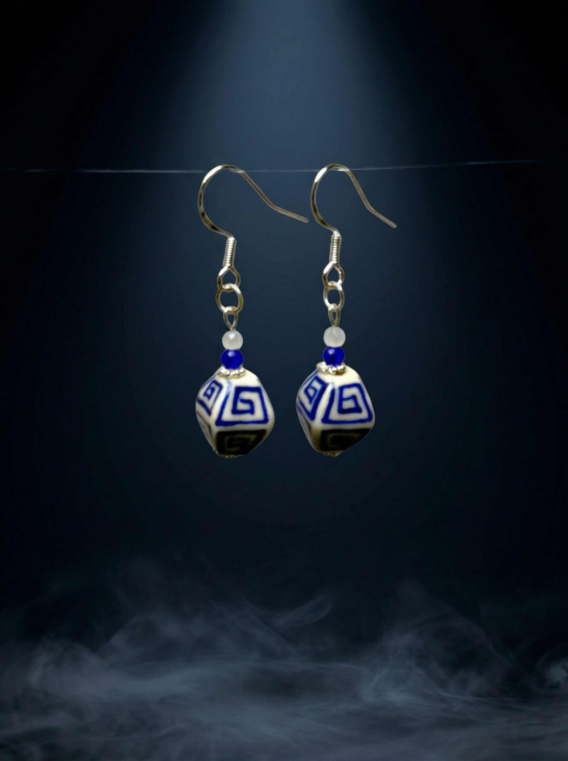 HECROWN blue floral ceramic earring resting on a dark volcanic rock with moss. Showcasing the sincere wabi-sabi handmade jewelry style.