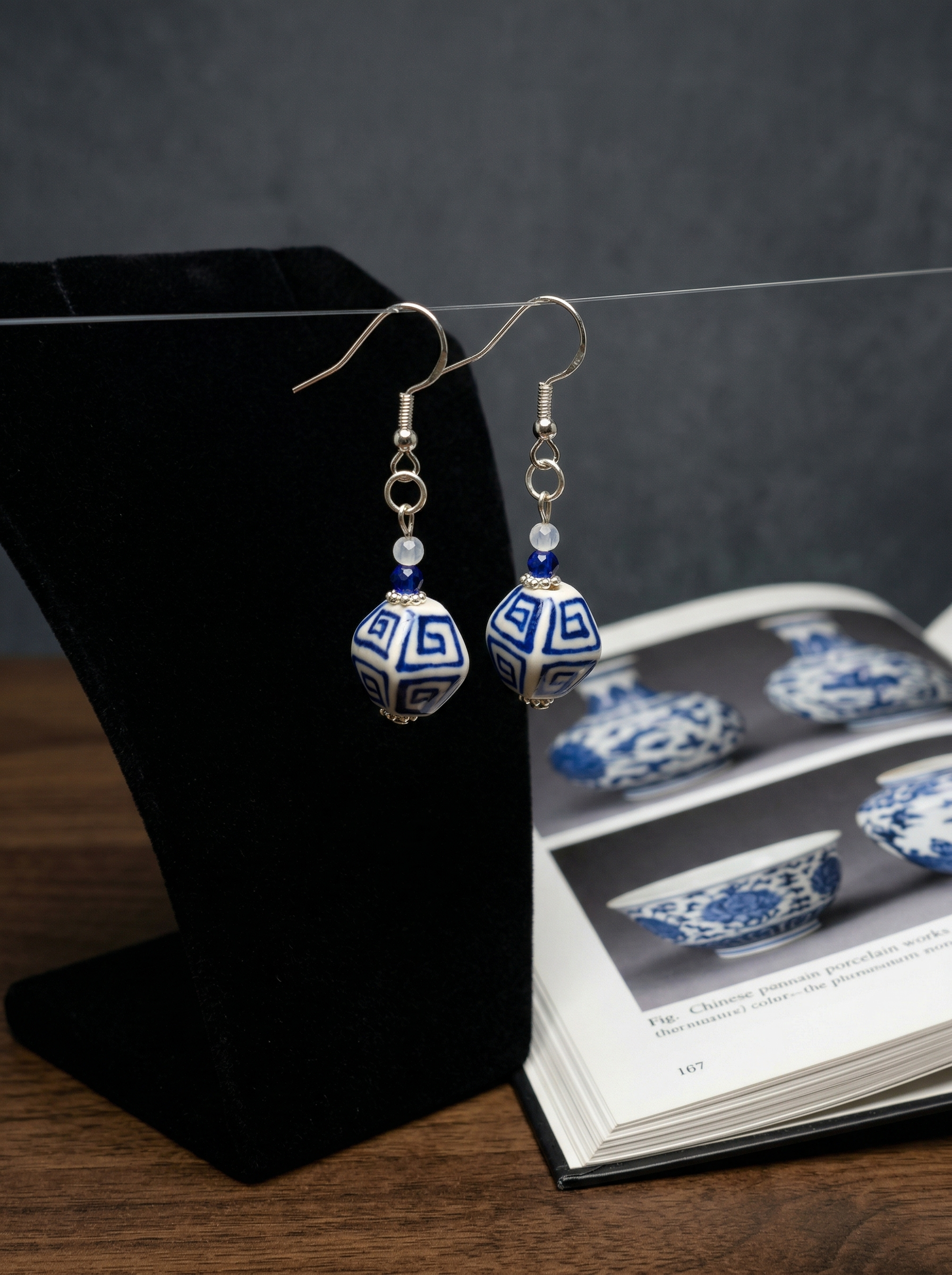 A pair of HECROWN blue floral ceramic hoop earrings displayed on white minimalist blocks. Sincere Jingdezhen ceramic art for modern lifestyle.