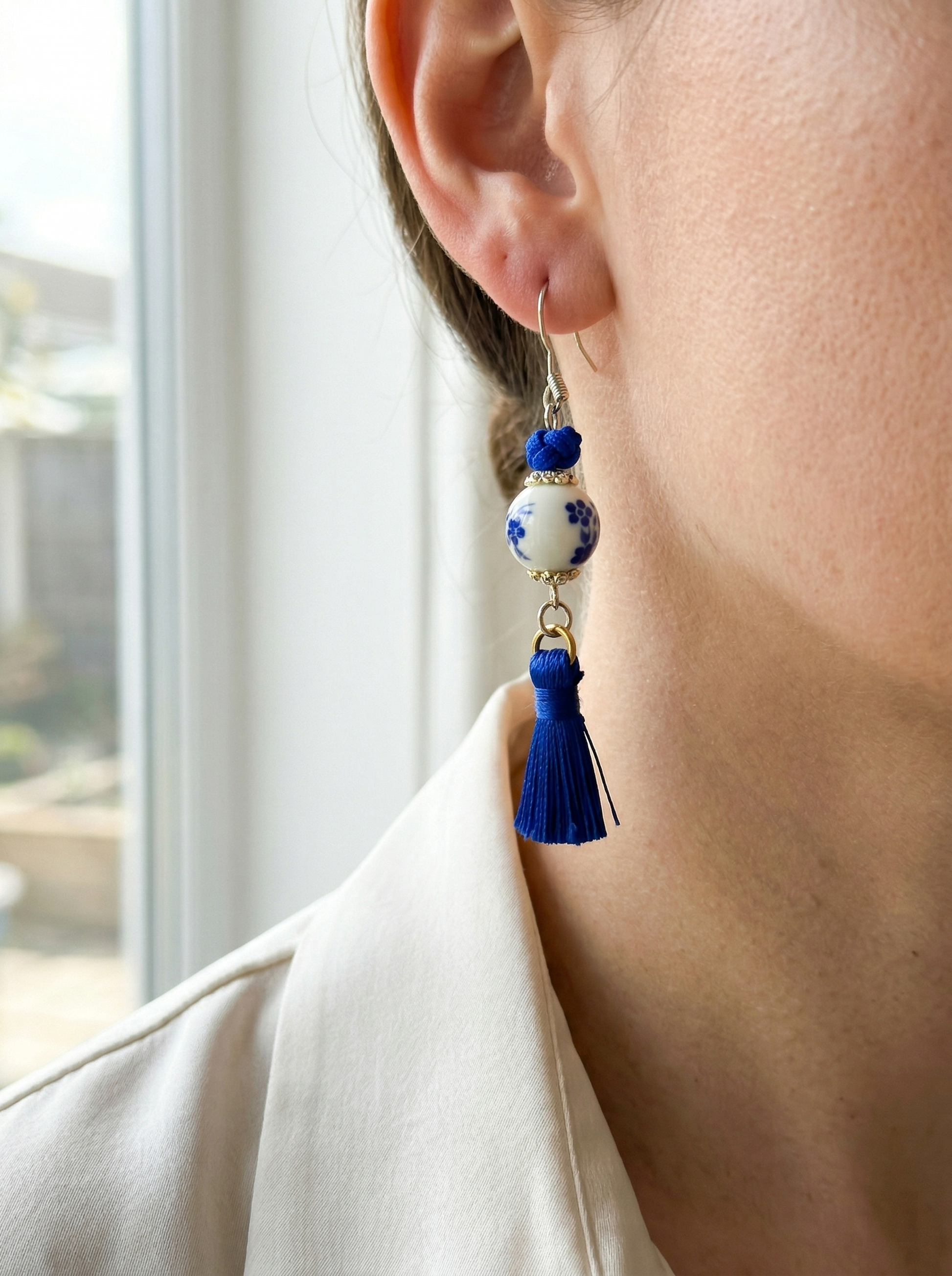 HECROWN handcrafted silk tassel and porcelain earrings hanging from a branch with leaf shadows. Sincere wabi-sabi handmade jewelry.