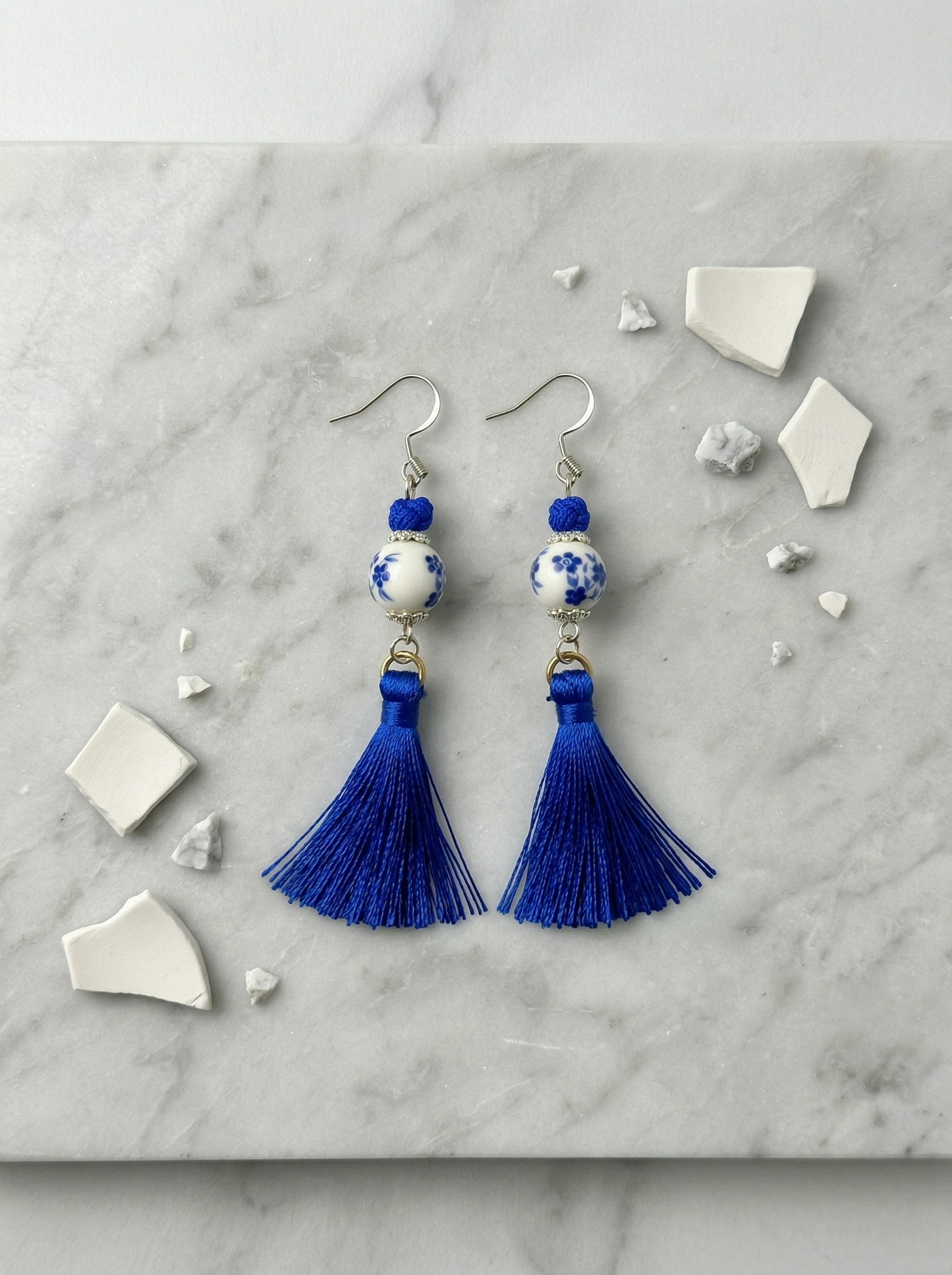 A pair of HECROWN 024 blue floral ceramic earrings with long silk tassels on a gold stand. Authentic Jingdezhen handmade jewelry.
