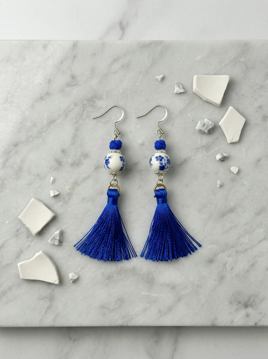 A pair of HECROWN 024 blue floral ceramic earrings with long silk tassels on a gold stand. Authentic Jingdezhen handmade jewelry.