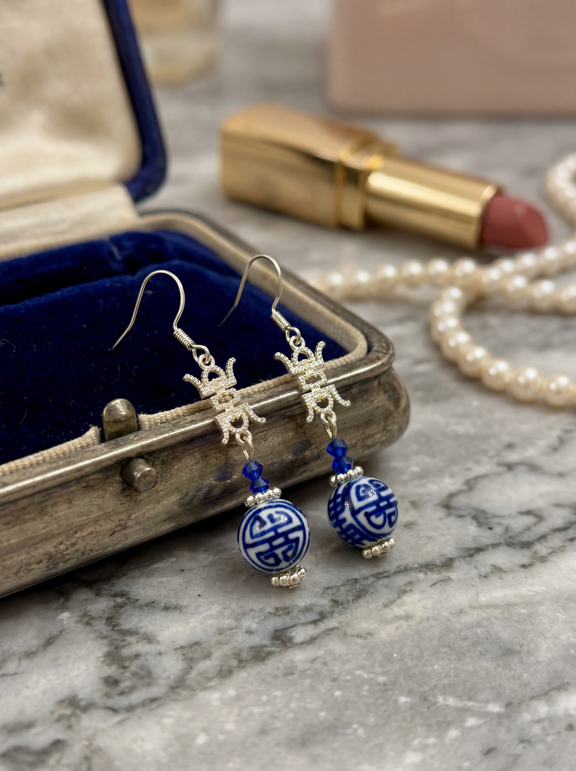 A single HECROWN blue ceramic flower bud earring hanging from a tree branch with soft shadows. Nature-inspired handmade ceramic gift and a soulful piece.