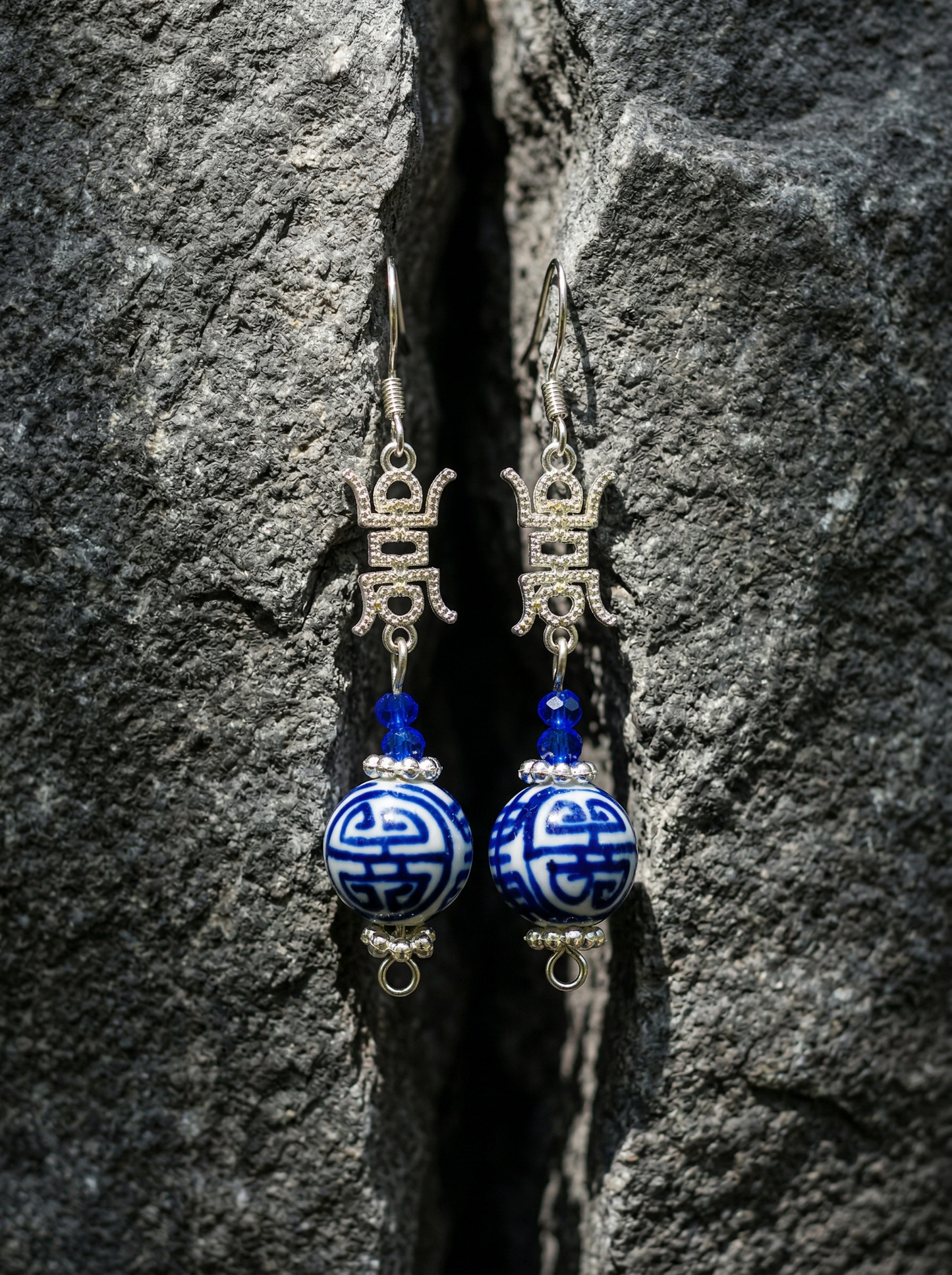 HECROWN 3D blue ceramic bloom bud earrings hanging on a gold T-stand against a clean background. Highlighting authentic handcrafted porcelain jewelry.