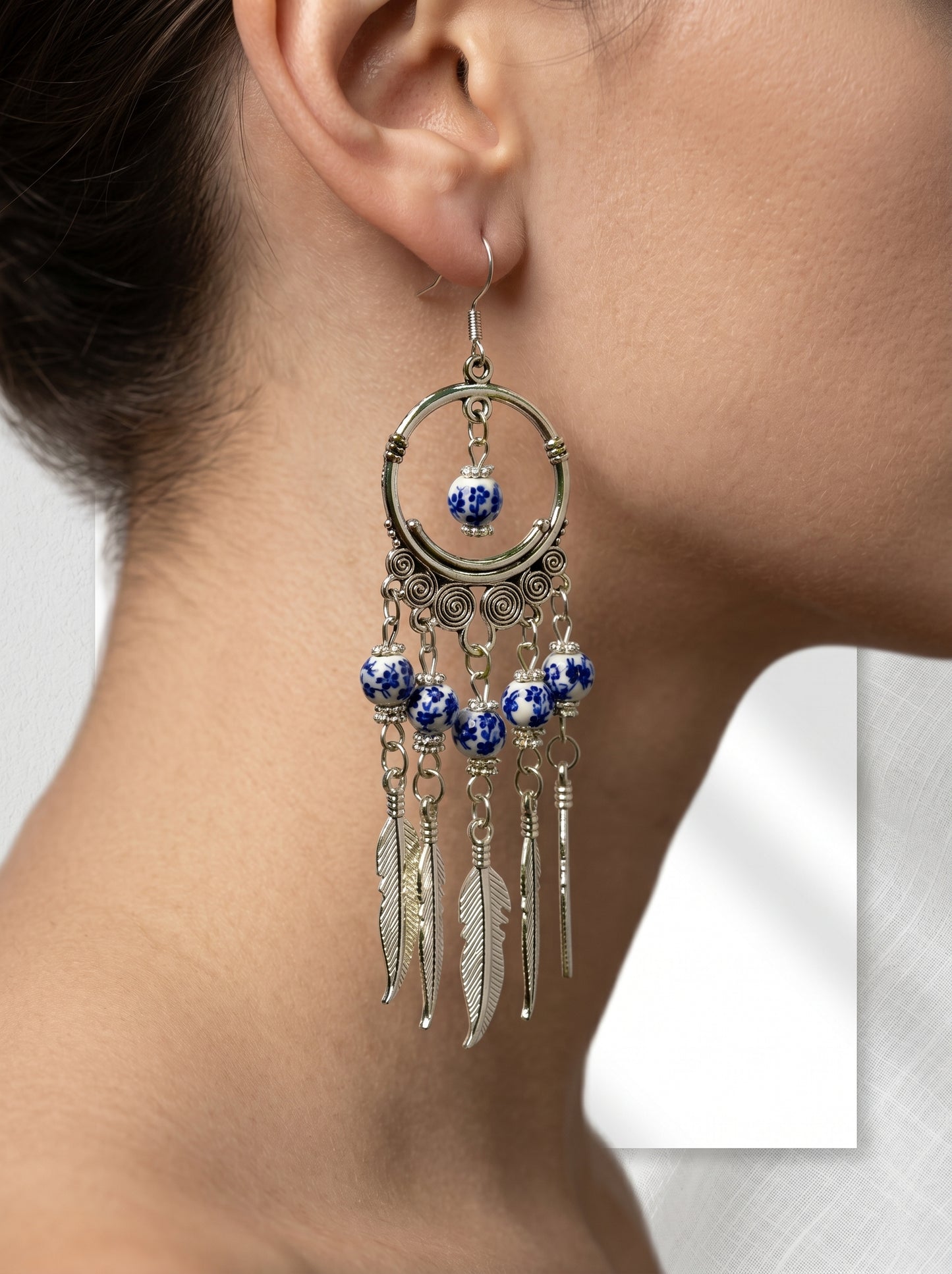 HECROWN handcrafted blue phantom ceramic earrings against a white wall with blind shadows. Highlighting the tranquil wabi-sabi handmade jewelry aesthetic.
