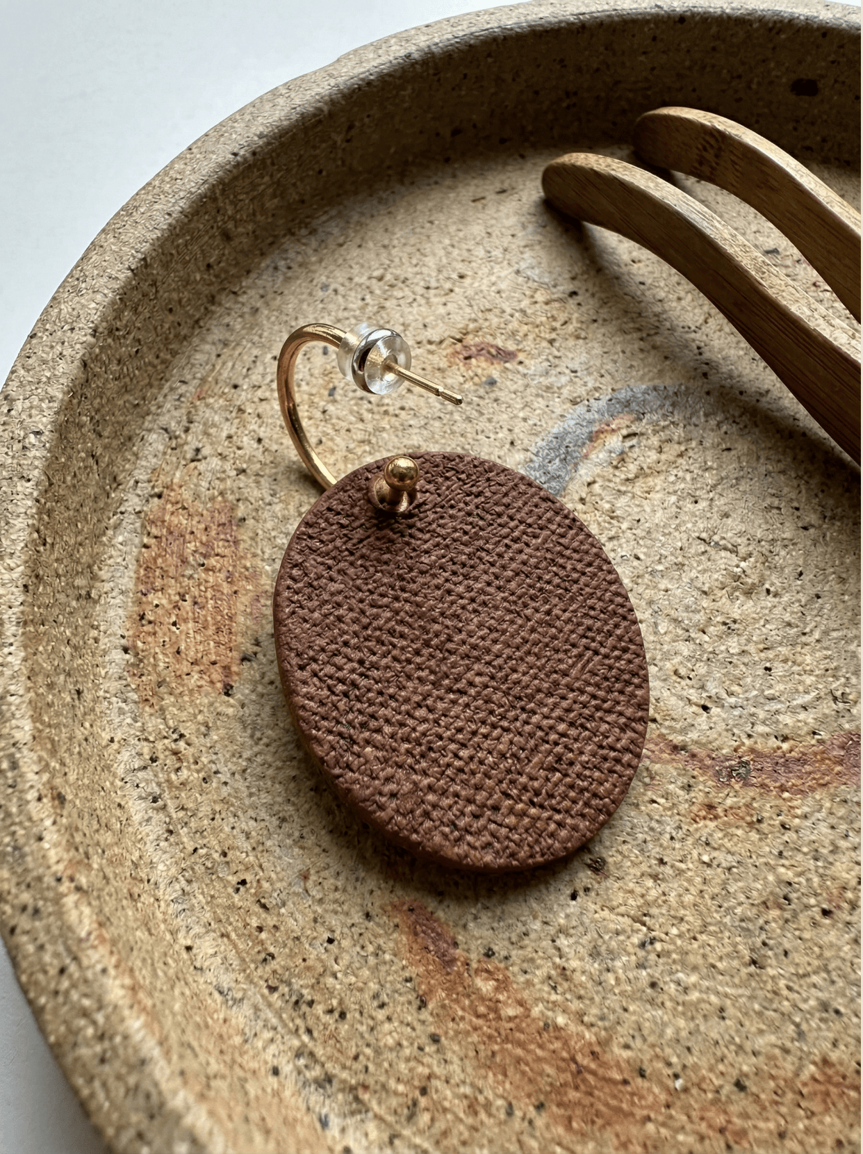 Detail view of the back of a handmade HECROWN ceramic earring, showcasing a unique brown fabric-press texture and the S925 sterling silver hoop. Displayed on a rustic pottery tray to emphasize the authentic craftsmanship and tactile quality of Jingdezhen ceramics.