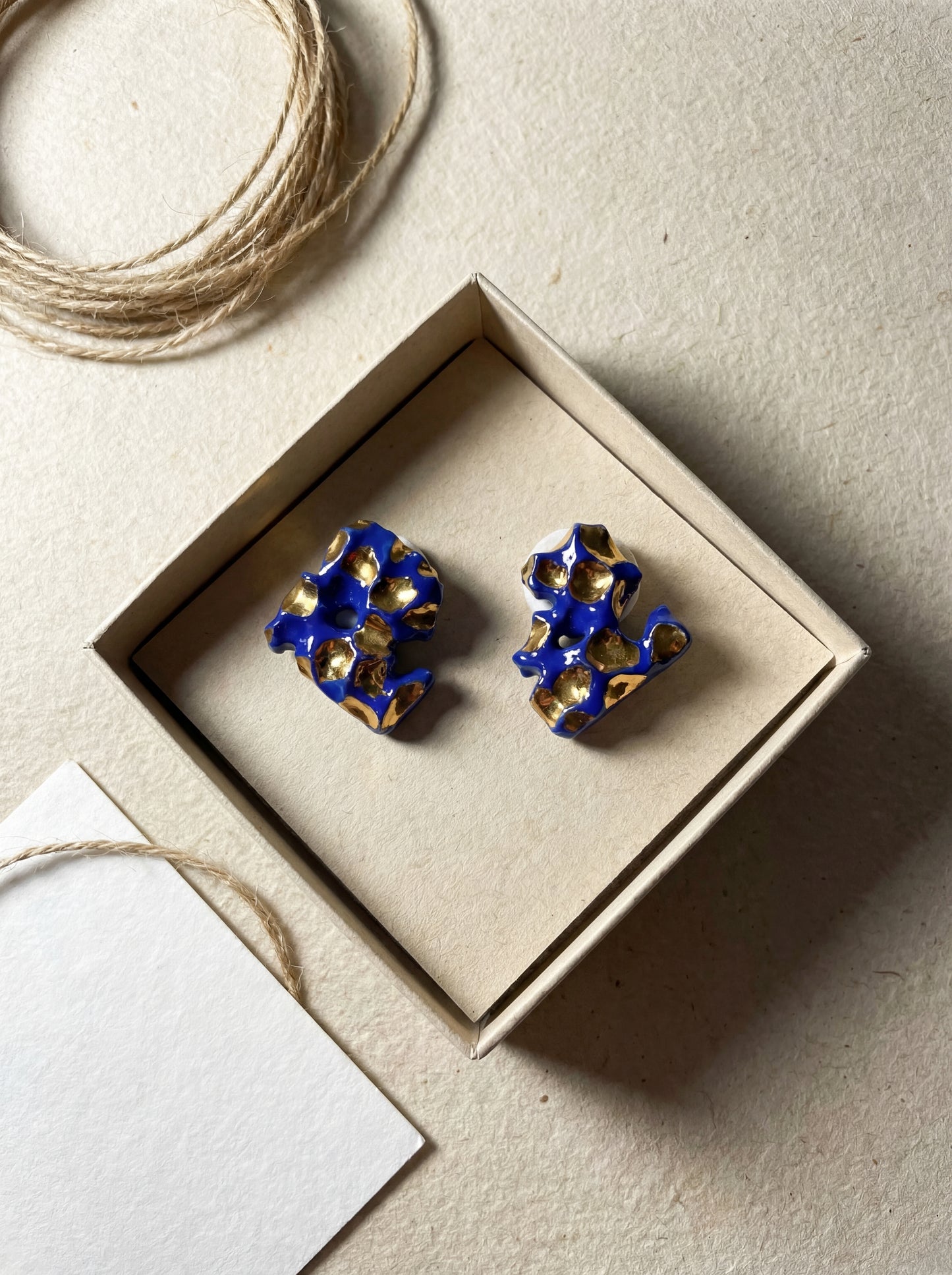 Top-down view of HECROWN 004 organic ceramic earrings in a sustainable kraft paper jewelry box, paired with natural twine and a white thank-you card. Representing the sincere, handcrafted unboxing experience of Jingdezhen artisan jewelry.