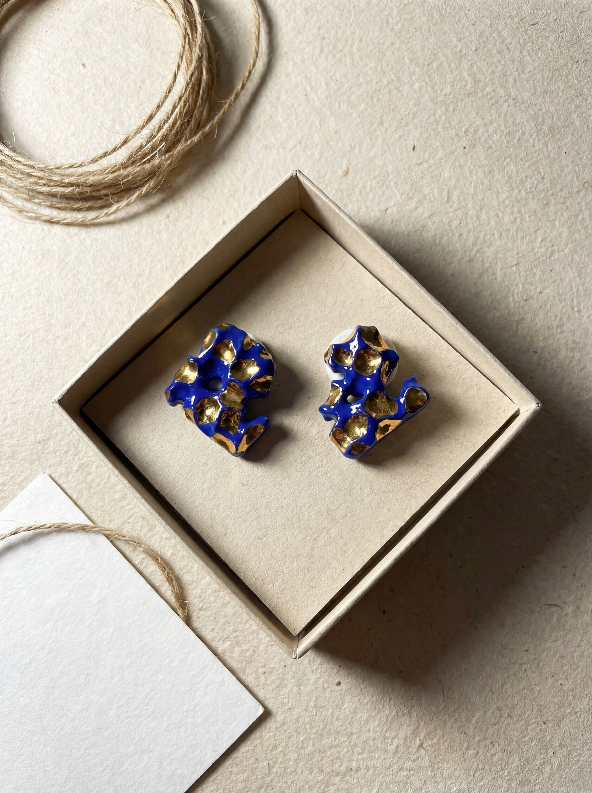 Top-down view of HECROWN 004 organic ceramic earrings in a sustainable kraft paper jewelry box, paired with natural twine and a white thank-you card. Representing the sincere, handcrafted unboxing experience of Jingdezhen artisan jewelry.