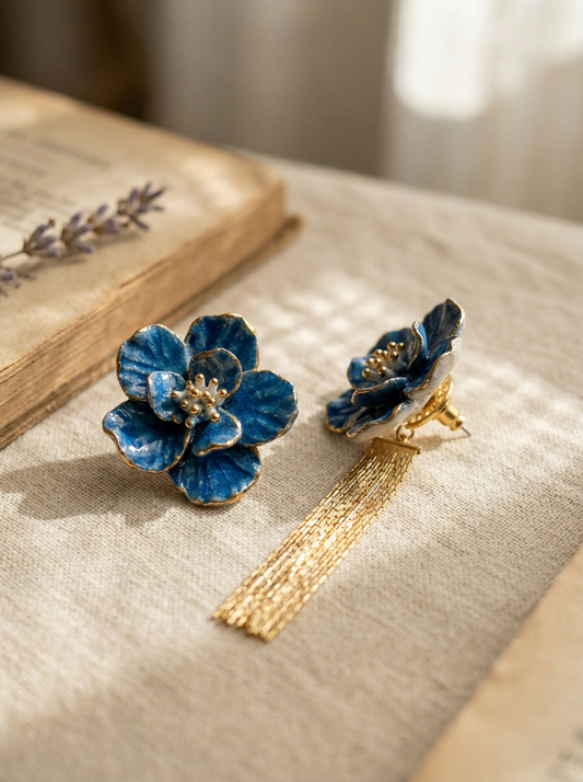 A pair of handcrafted Blue Bloom tassel earrings on a linen surface by an old book. These Jingdezhen ceramic earrings feature intricate blue petals and gold tassels, making them a perfect anniversary gift.