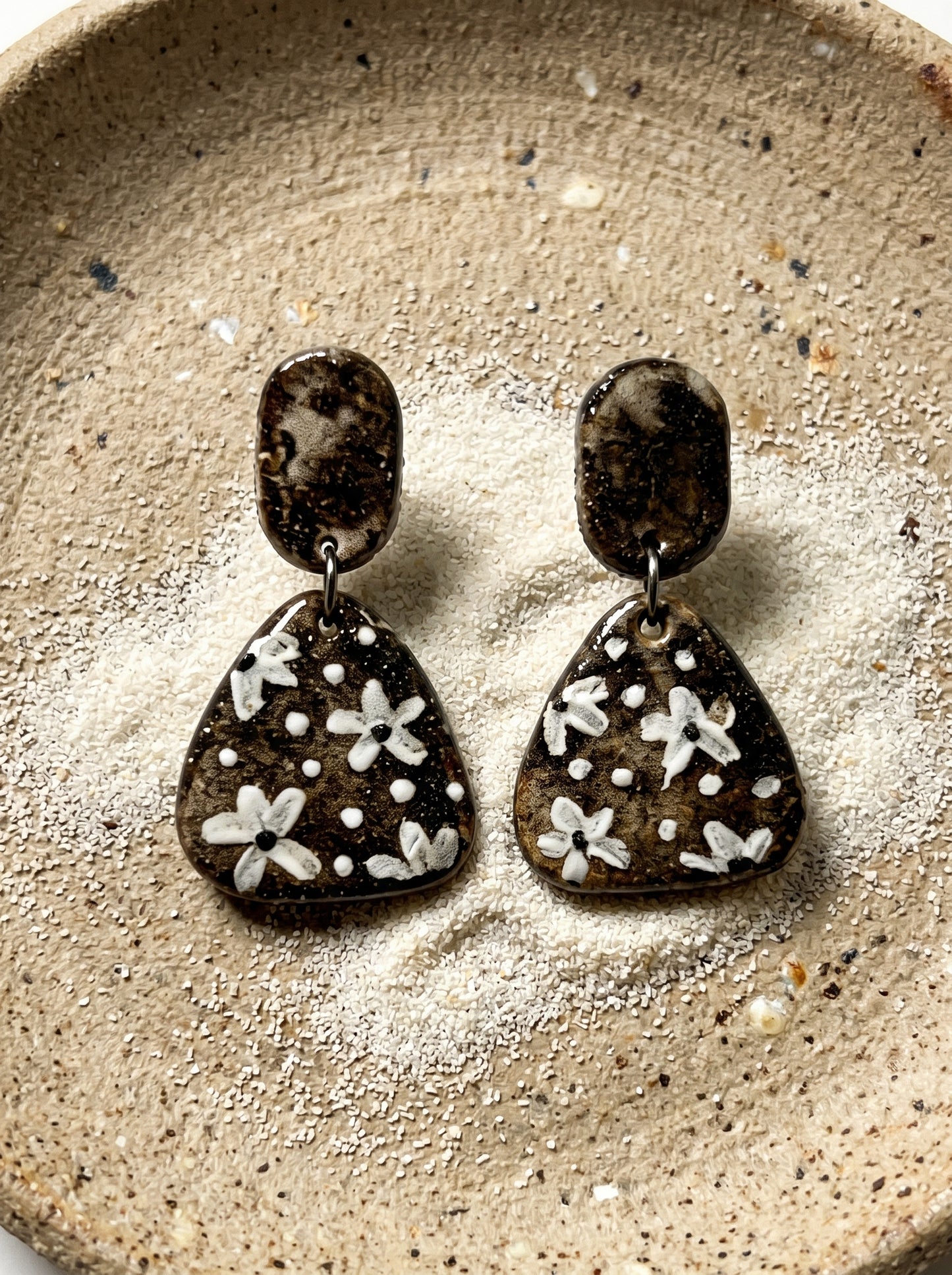 HECROWN round speckled ceramic earrings with black hammered tops resting on a wooden tray next to a coffee cup. A warm lifestyle shot of Jingdezhen handmade jewelry.