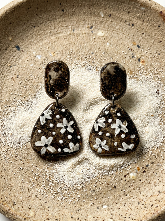HECROWN round speckled ceramic earrings with black hammered tops resting on a wooden tray next to a coffee cup. A warm lifestyle shot of Jingdezhen handmade jewelry.