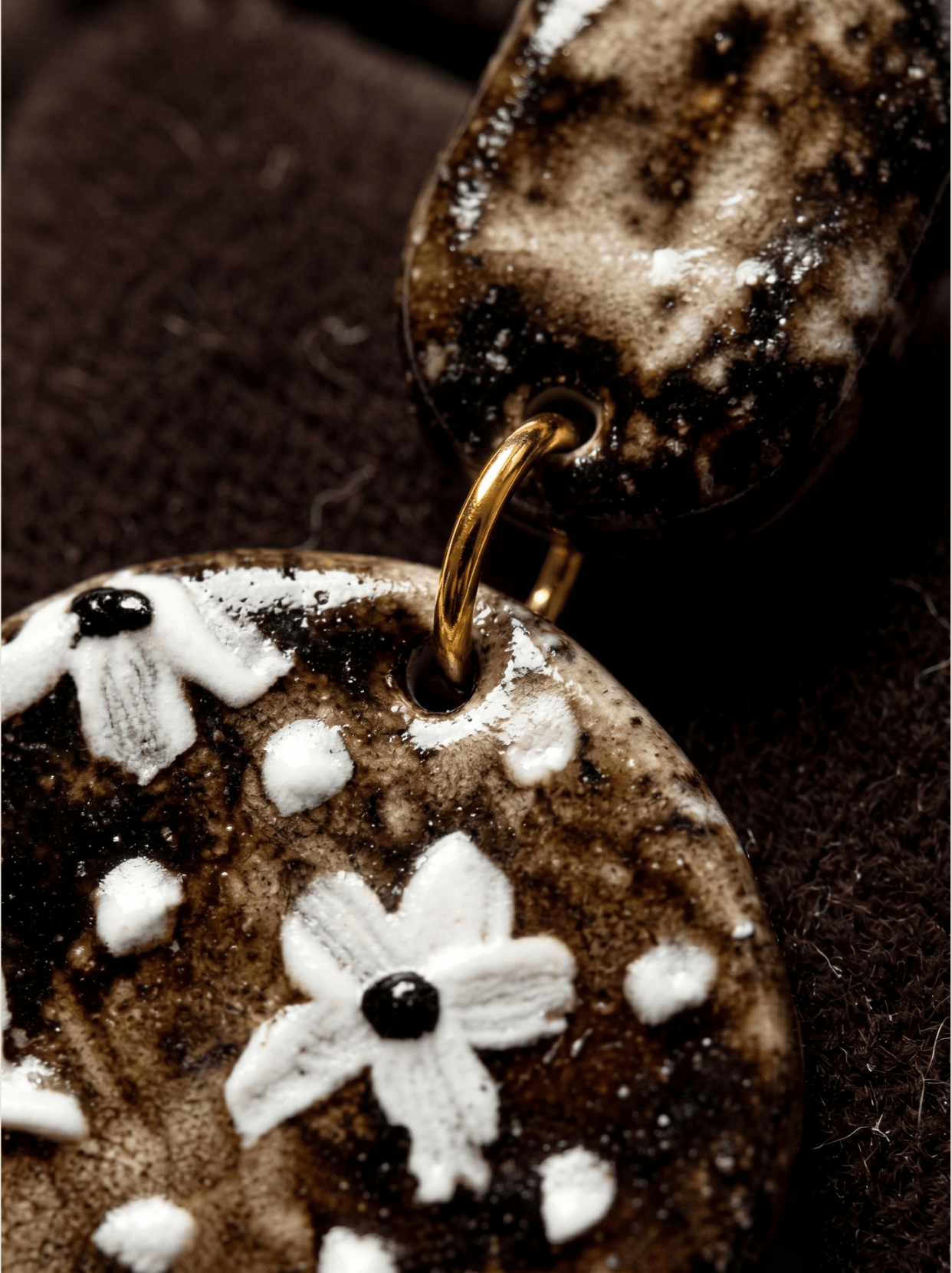 Extreme macro close-up of a HECROWN vintage ceramic earring. Raised white hand-painted flowers on a dark crackle glaze with a gold connecting ring. Authentic Jingdezhen handmade jewelry.